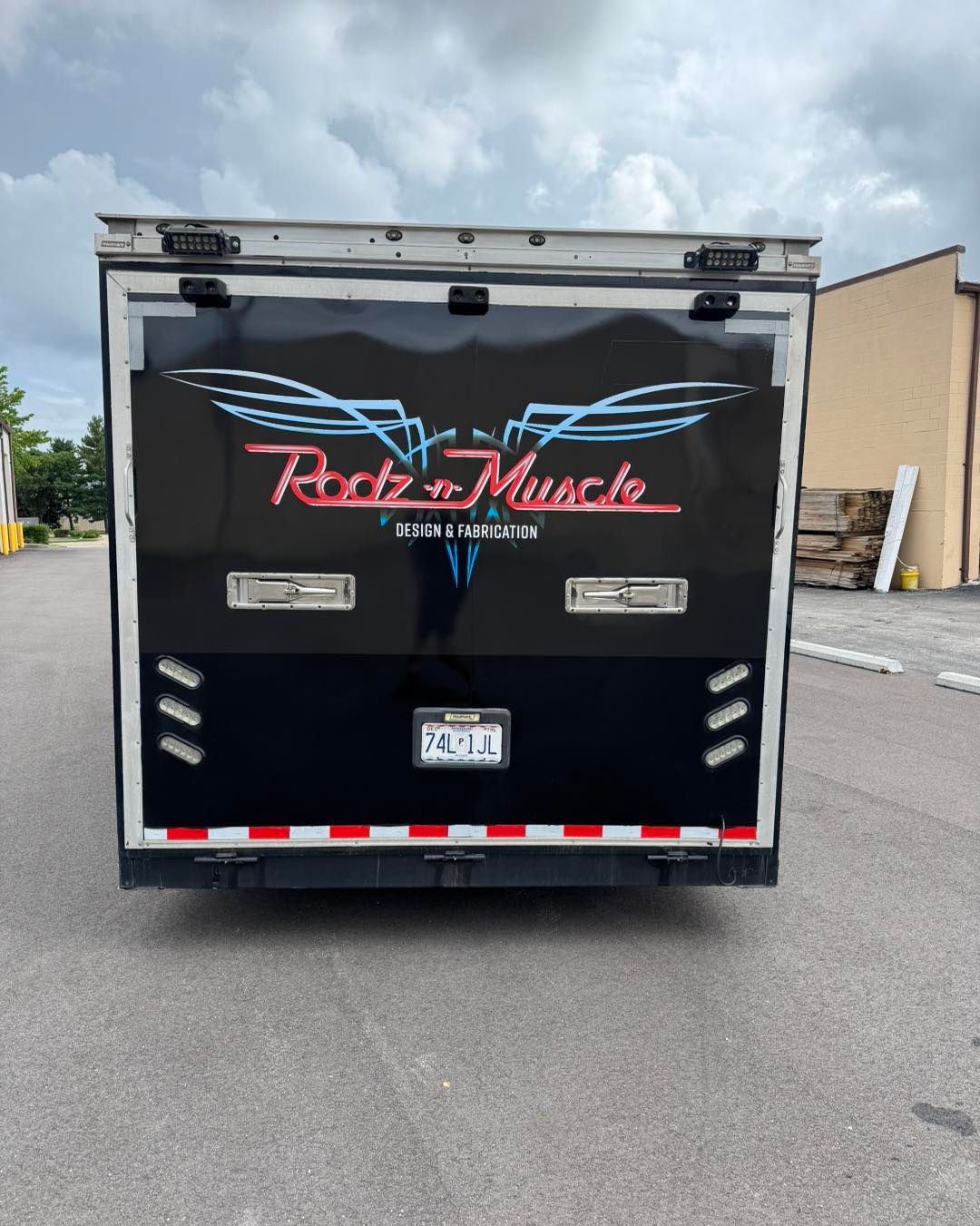 Black box trailer with “Rods 2 Muscle” logo parked on a street under cloudy skies
