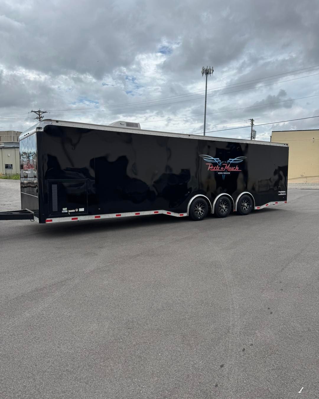 Black enclosed cargo trailer with three axles parked in a lot under cloudy skies