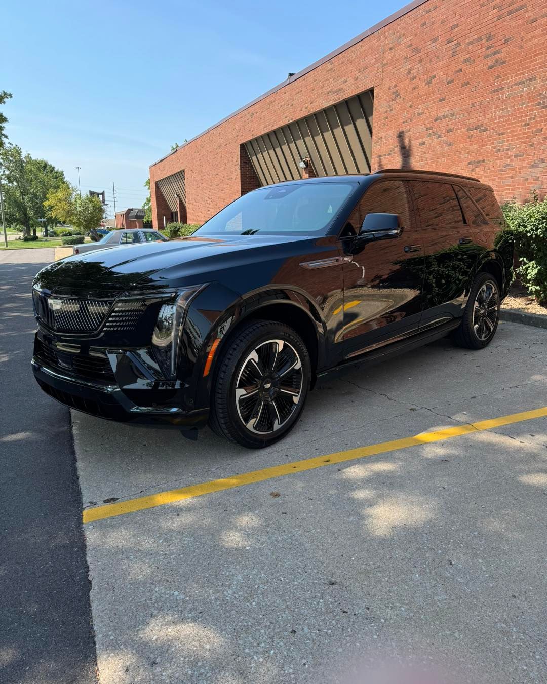 Black SUV parked beside a brick building on a sunny street.