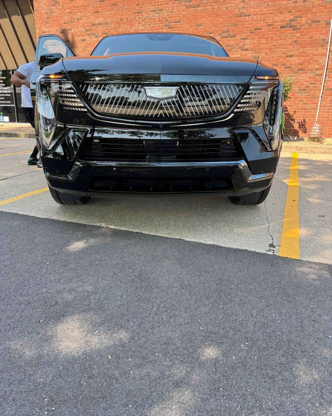 Black SUV parked in a lot beside a brick wall, front view with grille damaged and one door open