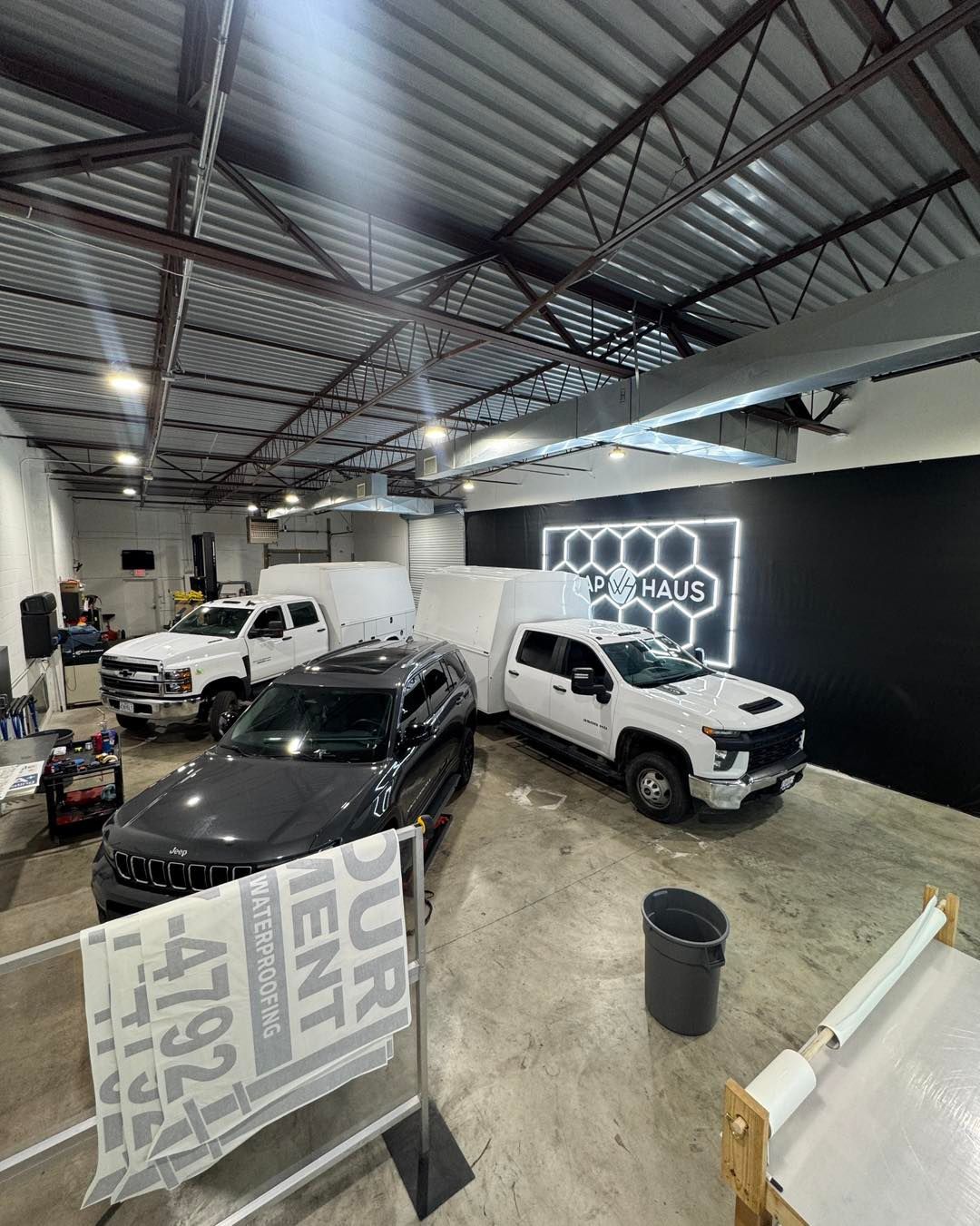 Car showroom with several cars under a metal roof and a glowing wall sign in the back.