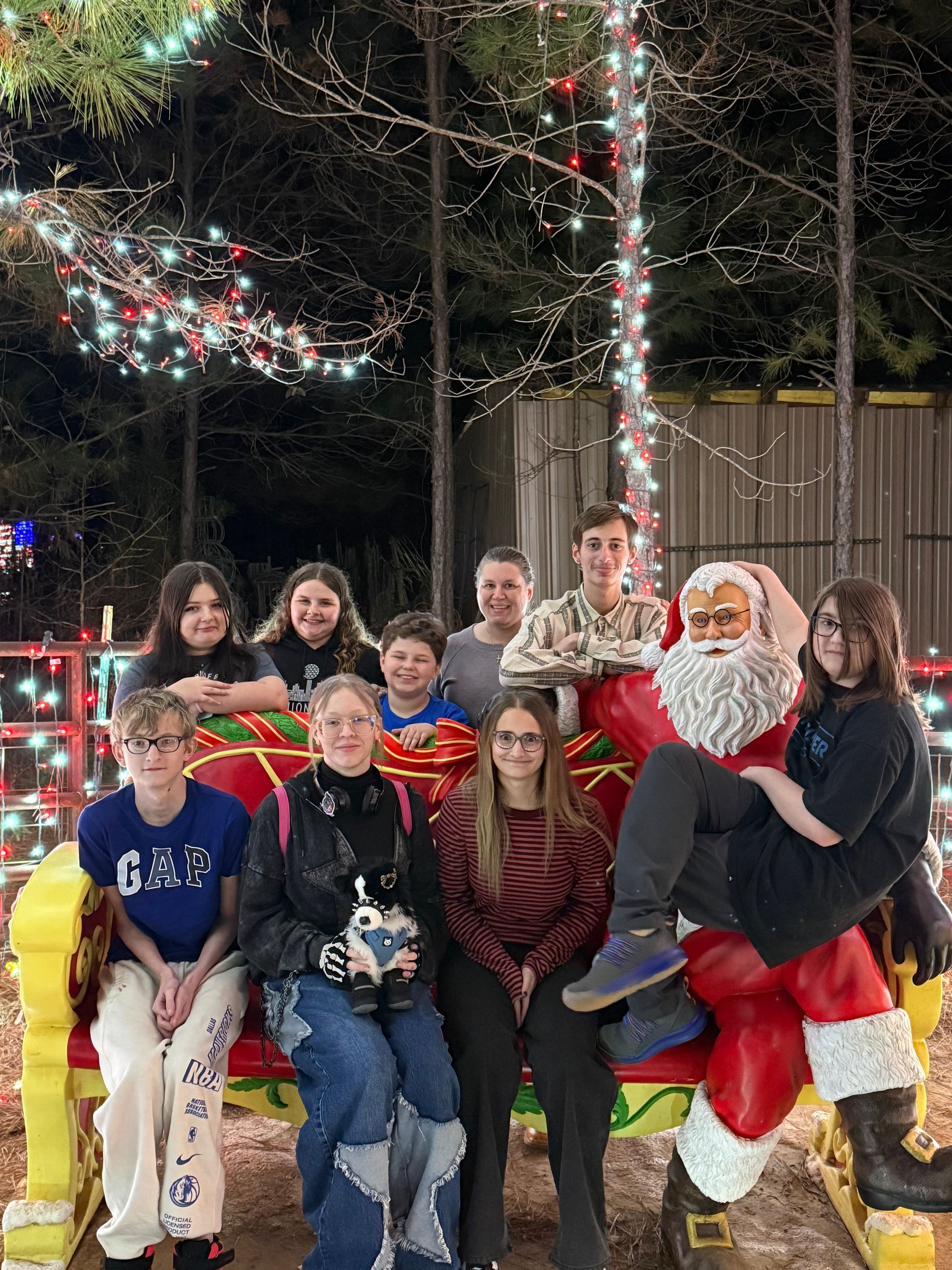 Group of people posing with a Santa statue and holiday lights.  Outdoors at night.