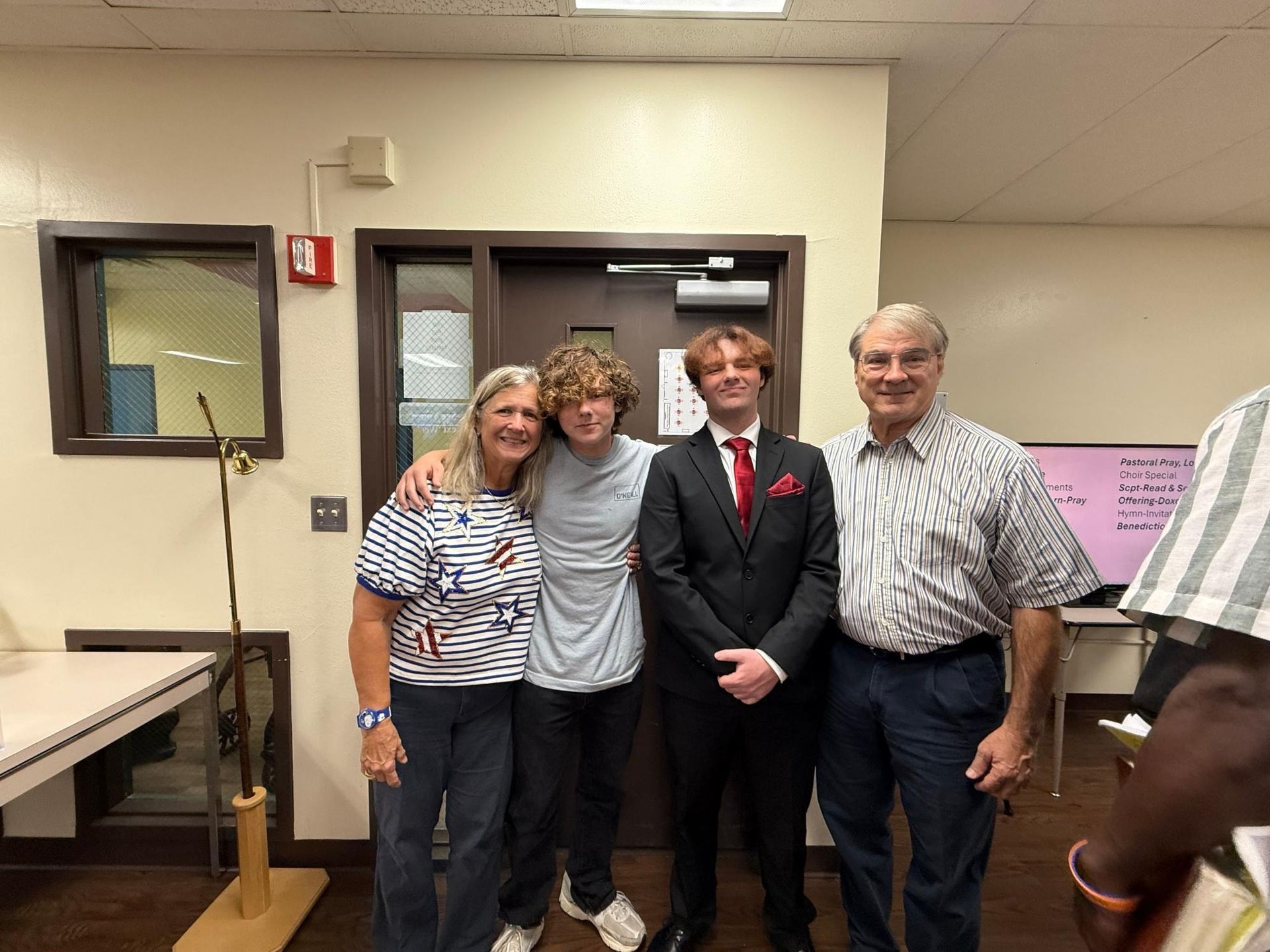 Family of four poses indoors; two young men, two older adults. One young man wears a suit. All smile.