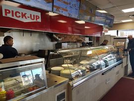 Restaurant counter with glass display cases and a red PICK-UP sign above menu boards
