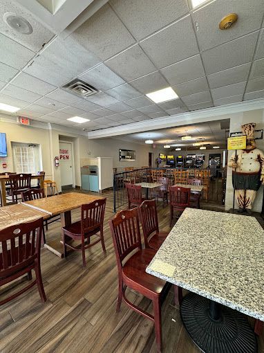 Empty restaurant dining room with wooden tables and chairs, patterned floor, and a ceiling fan overhead