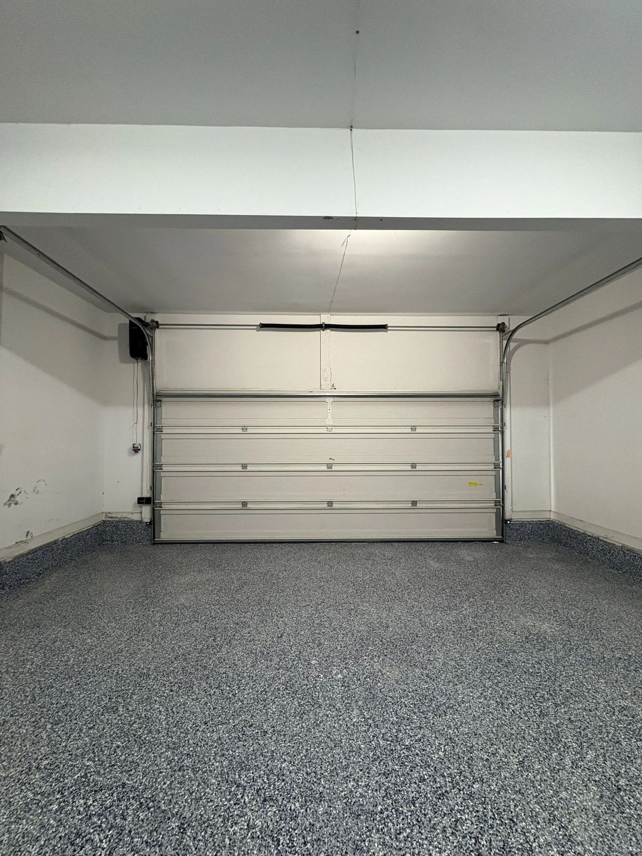 Empty white garage with a closed sectional door and speckled gray floor