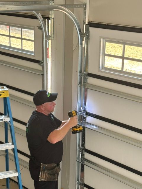 Technician installing metal conduit beside a garage door with a power tool