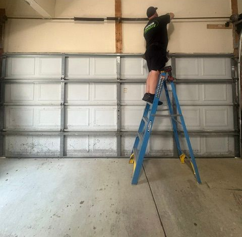 Person on a blue ladder adjusting a garage door opener rail in a garage