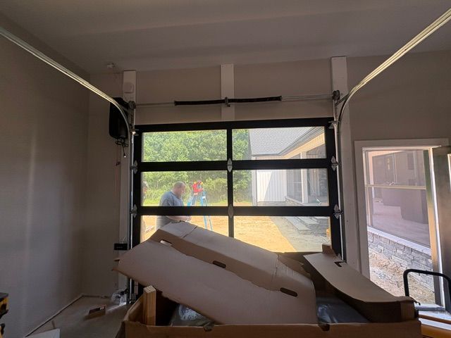 Inside a garage-like room, cardboard and debris are piled in front of a large windowed door.