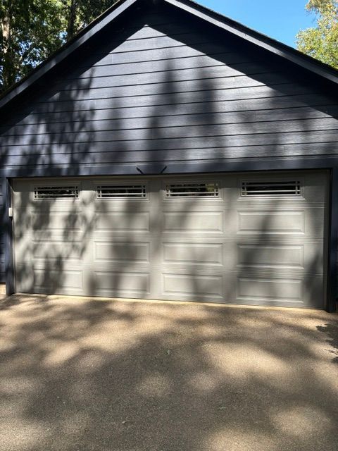 Gray two-car garage with white doors and blue siding, dappled by tree shadows in daylight