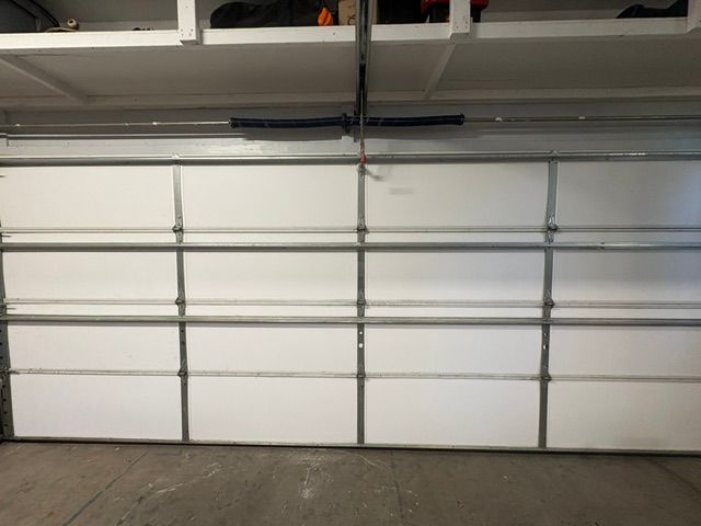 White garage door with metal panels and a gray concrete floor in a garage interior.
