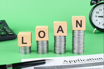 “Loan” word formed with wooden cubes on coin stack, symbolizing signature loan services.