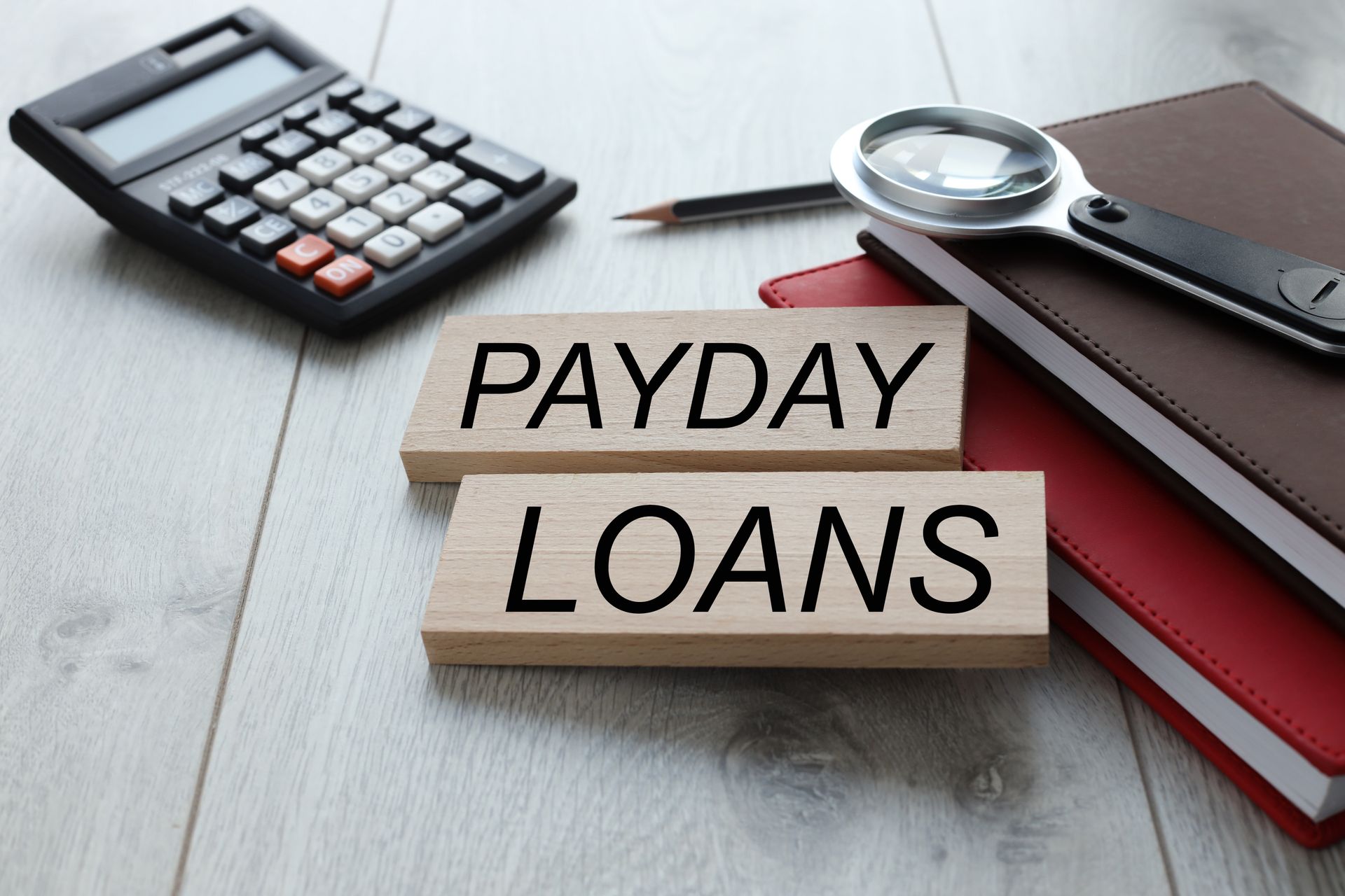 Desktop with notebooks, magnifying glass, and document about payday loan services. Desktop with notebooks, magnifying glass, and document about payday loan services.