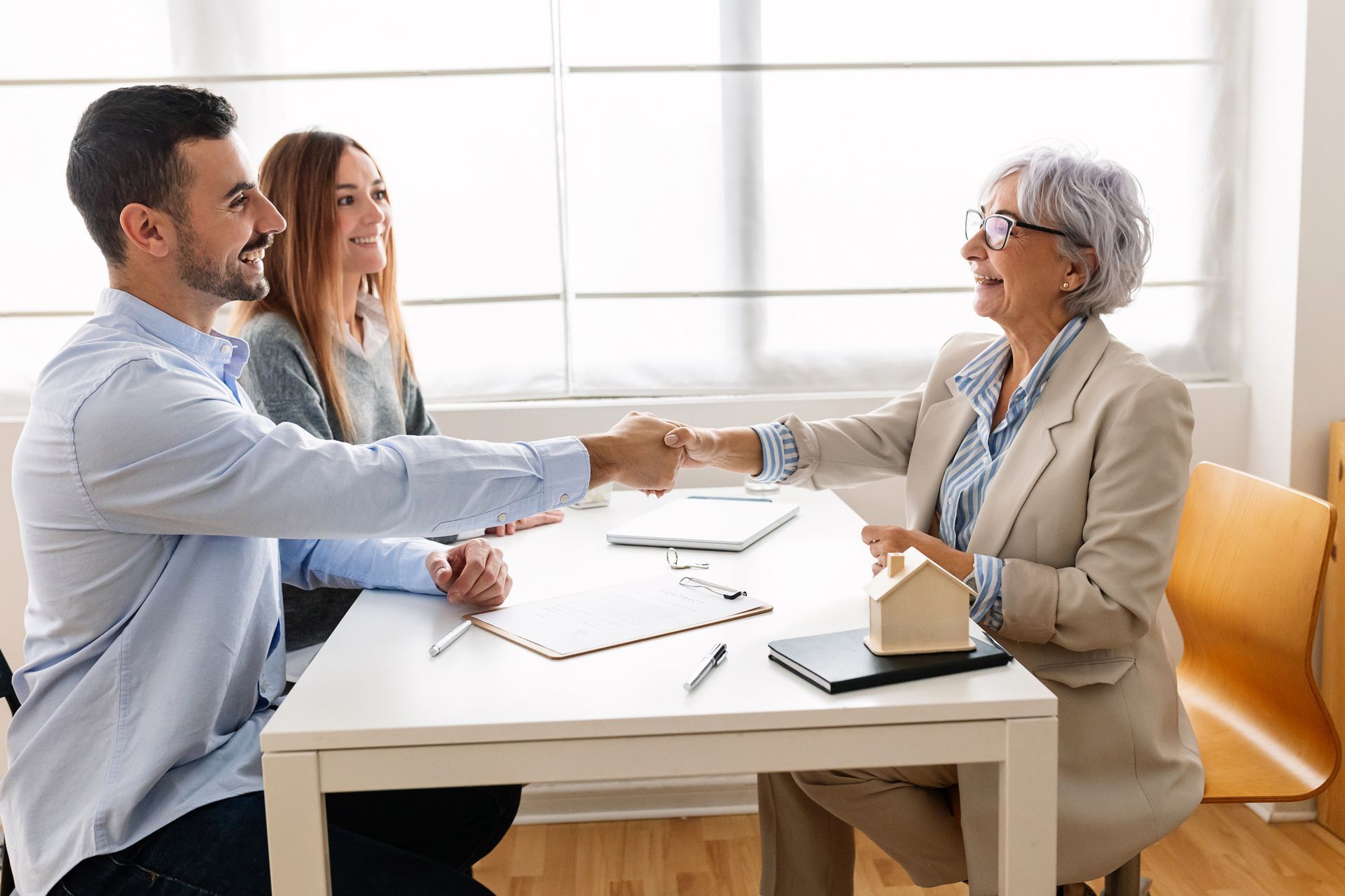 Smiling couple shaking hands with advisor after signature loan approval in office setting.