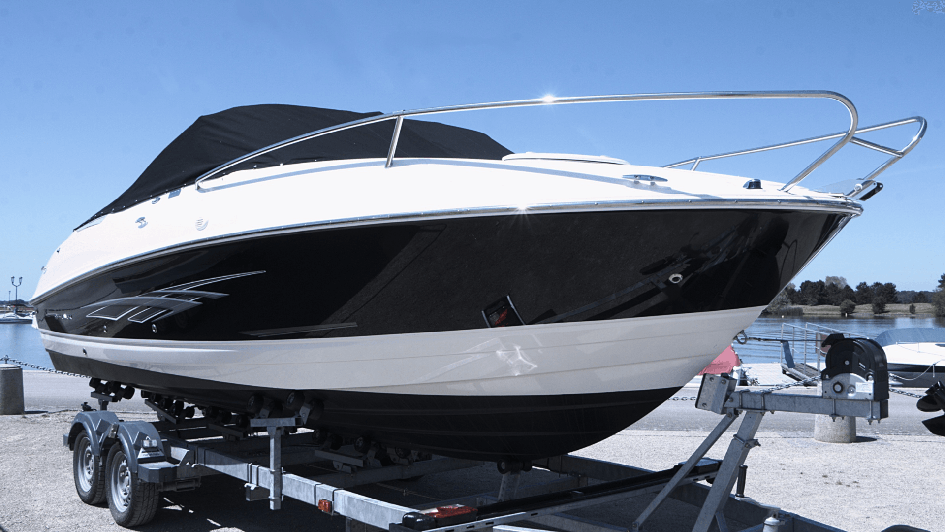 A boat is sitting on a trailer next to a body of water.
