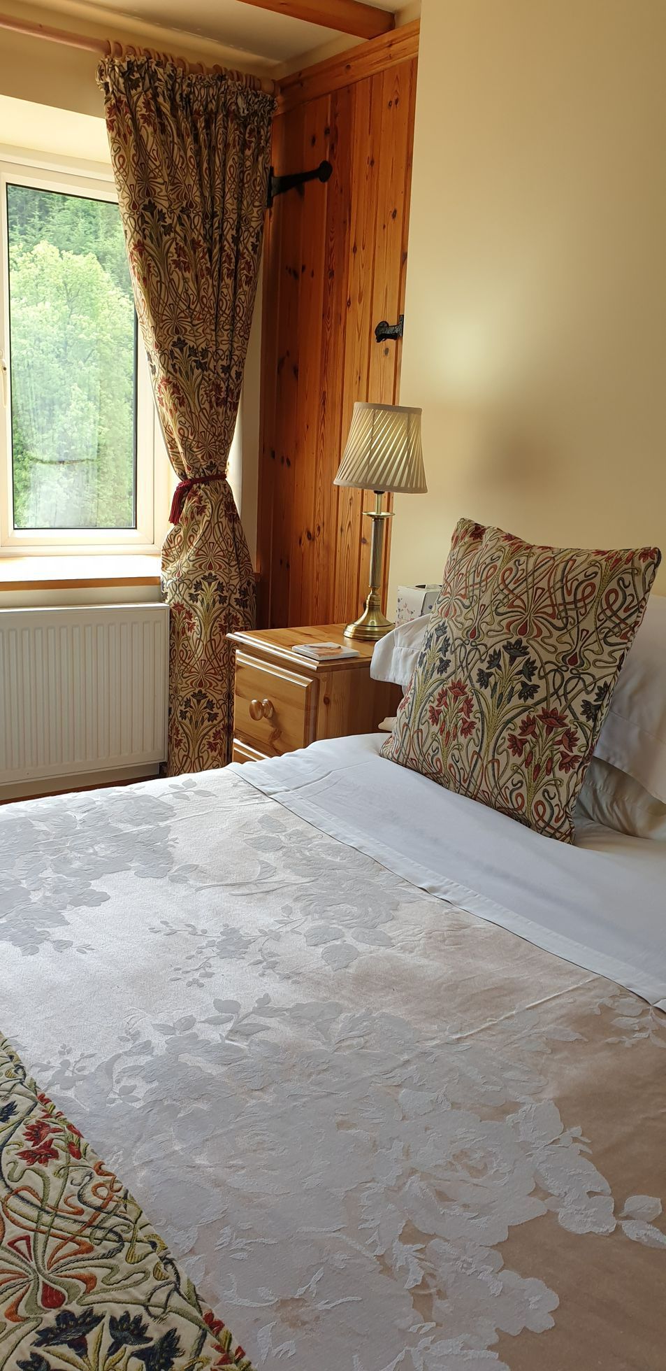 Bedroom with a patterned bedspread, pillow, and curtains near a window and wooden nightstand.