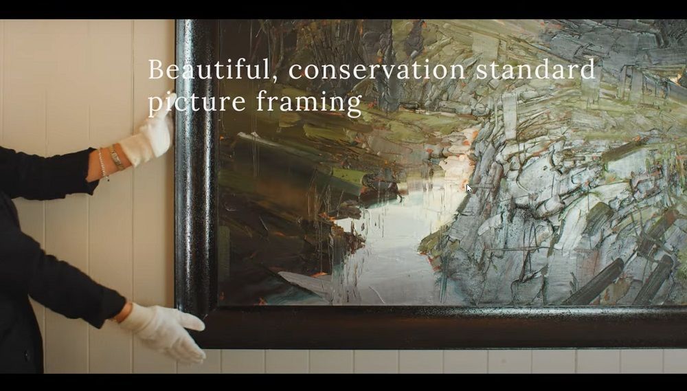An image of an ARTSHOP team member hanging a newly-framed large format landscape painting.
