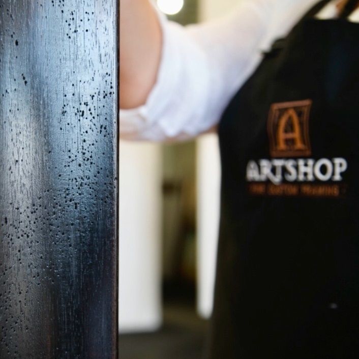 A close up of an artwork frame, with an ARTSHOP team members apron blurred standing in the background.