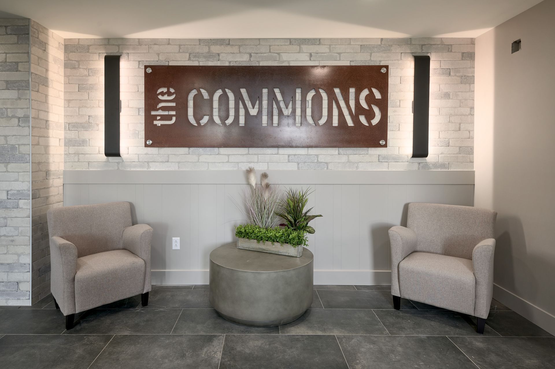 Lobby seating area with two beige chairs, a planter, and a “the COMMONS” wall sign