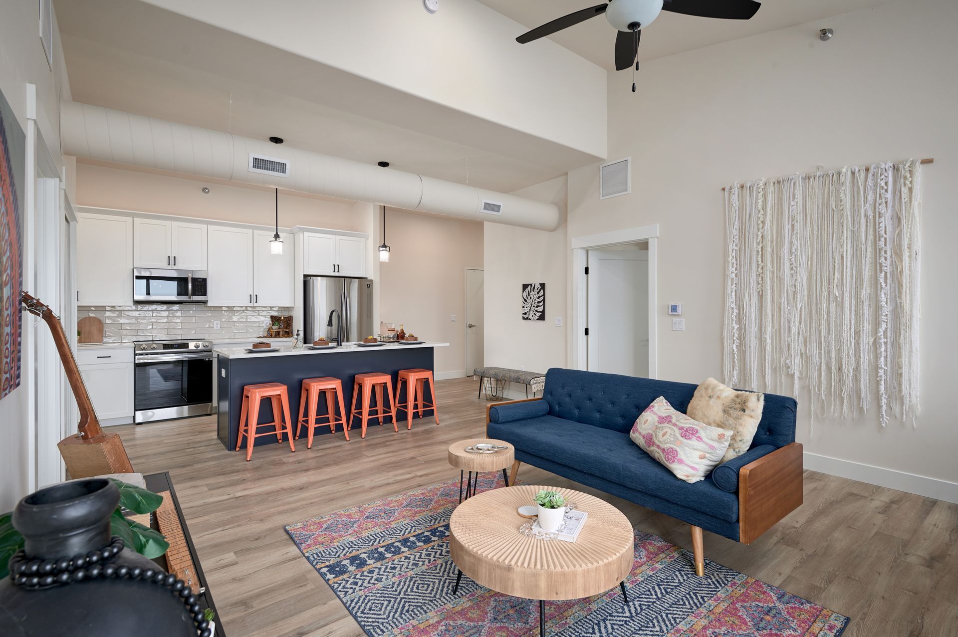 Open-concept living room and kitchen with blue sofa, patterned rug, island stools, and high ceilings