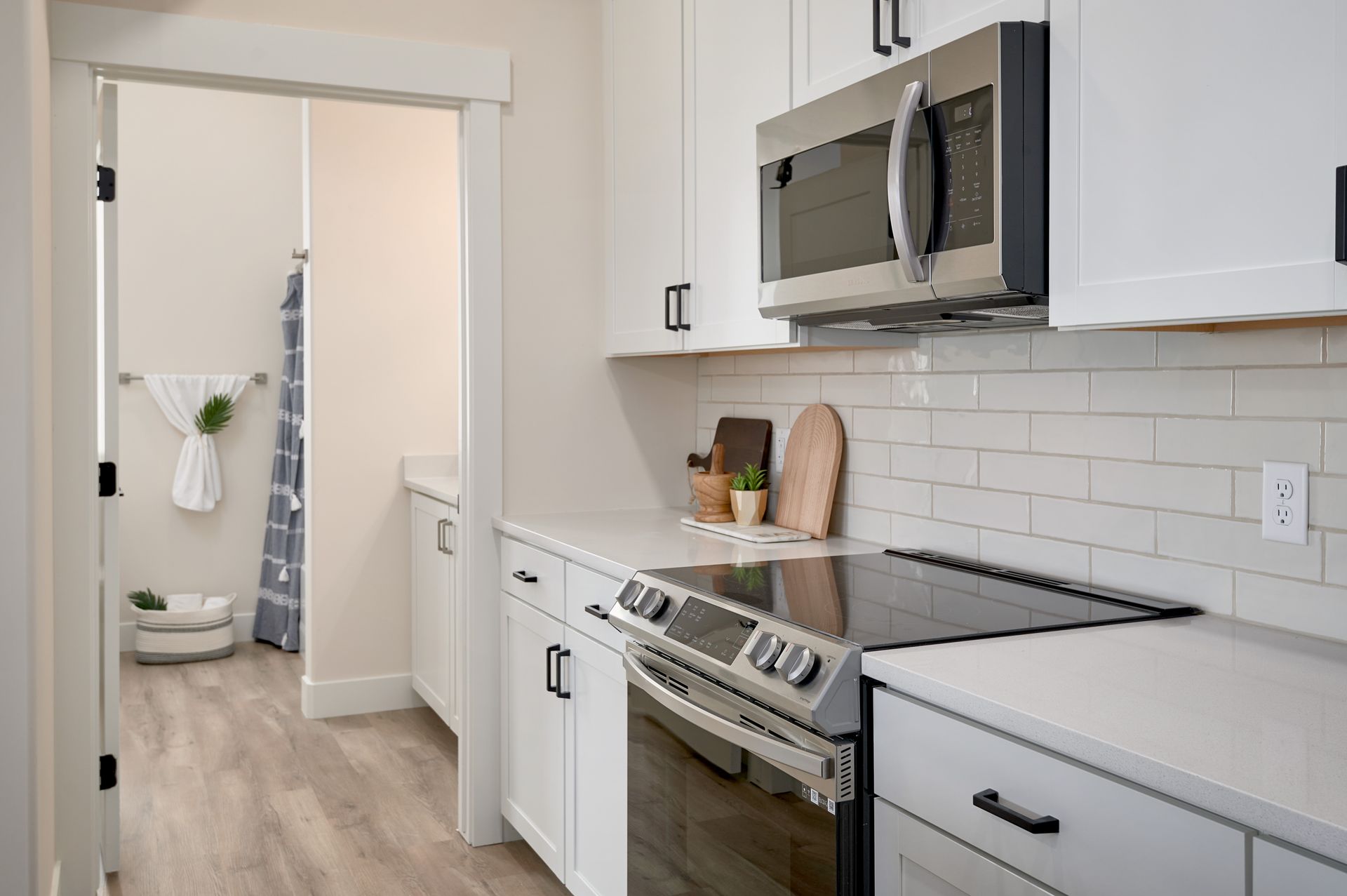 Modern kitchen with stainless steel stove and microwave, white cabinets, and a doorway to a hallway with decor.