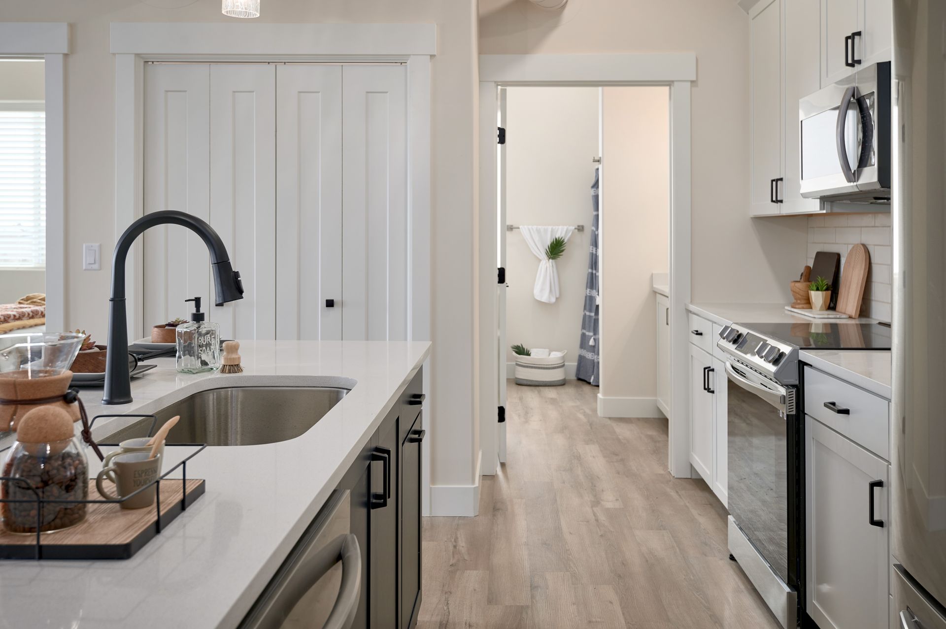 Bright modern kitchen with white cabinets, island sink, stainless appliances, and doorway to hallway