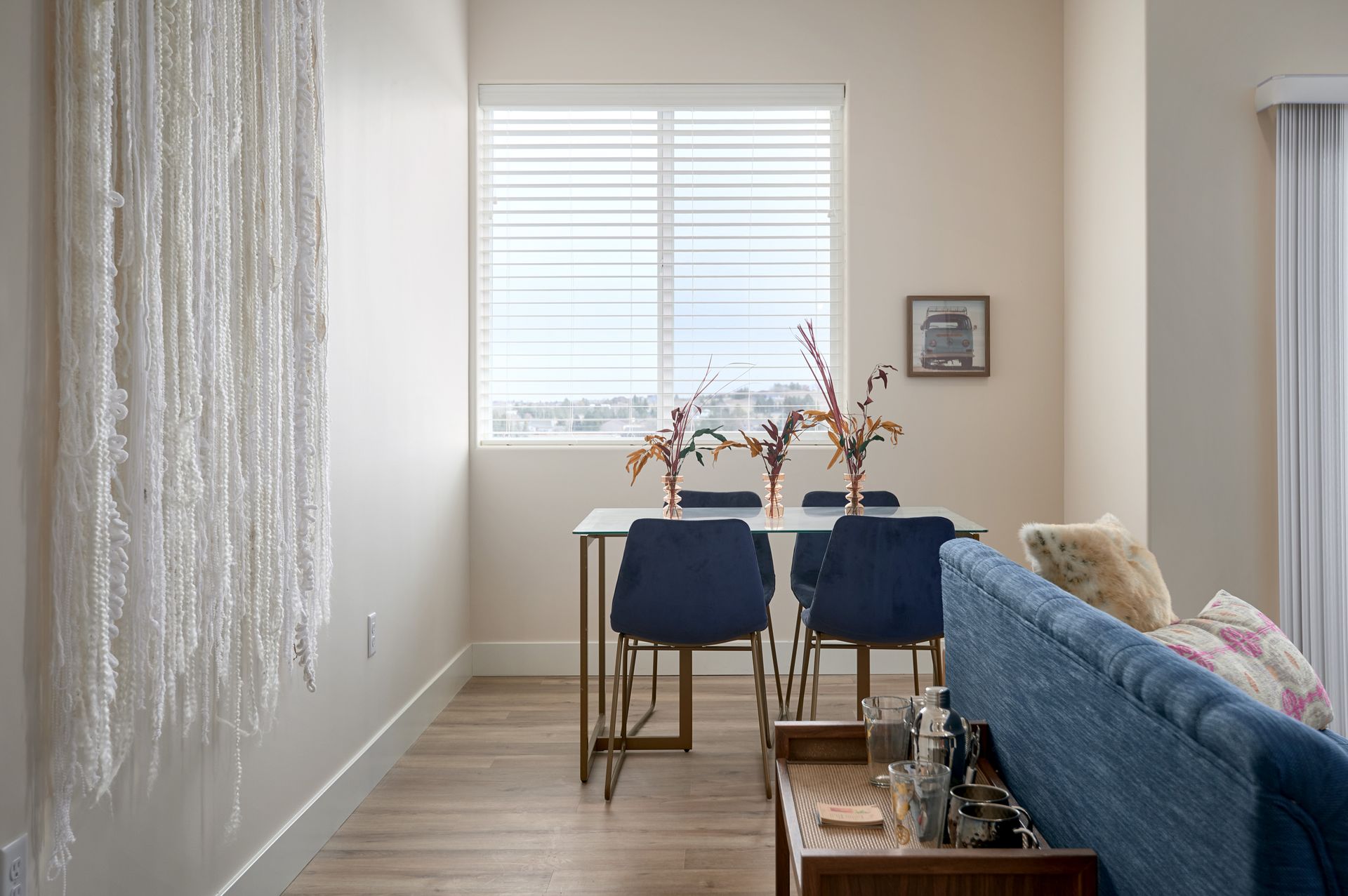 Dining area with blue chairs, a small table by a window, and a blue sofa in a bright room