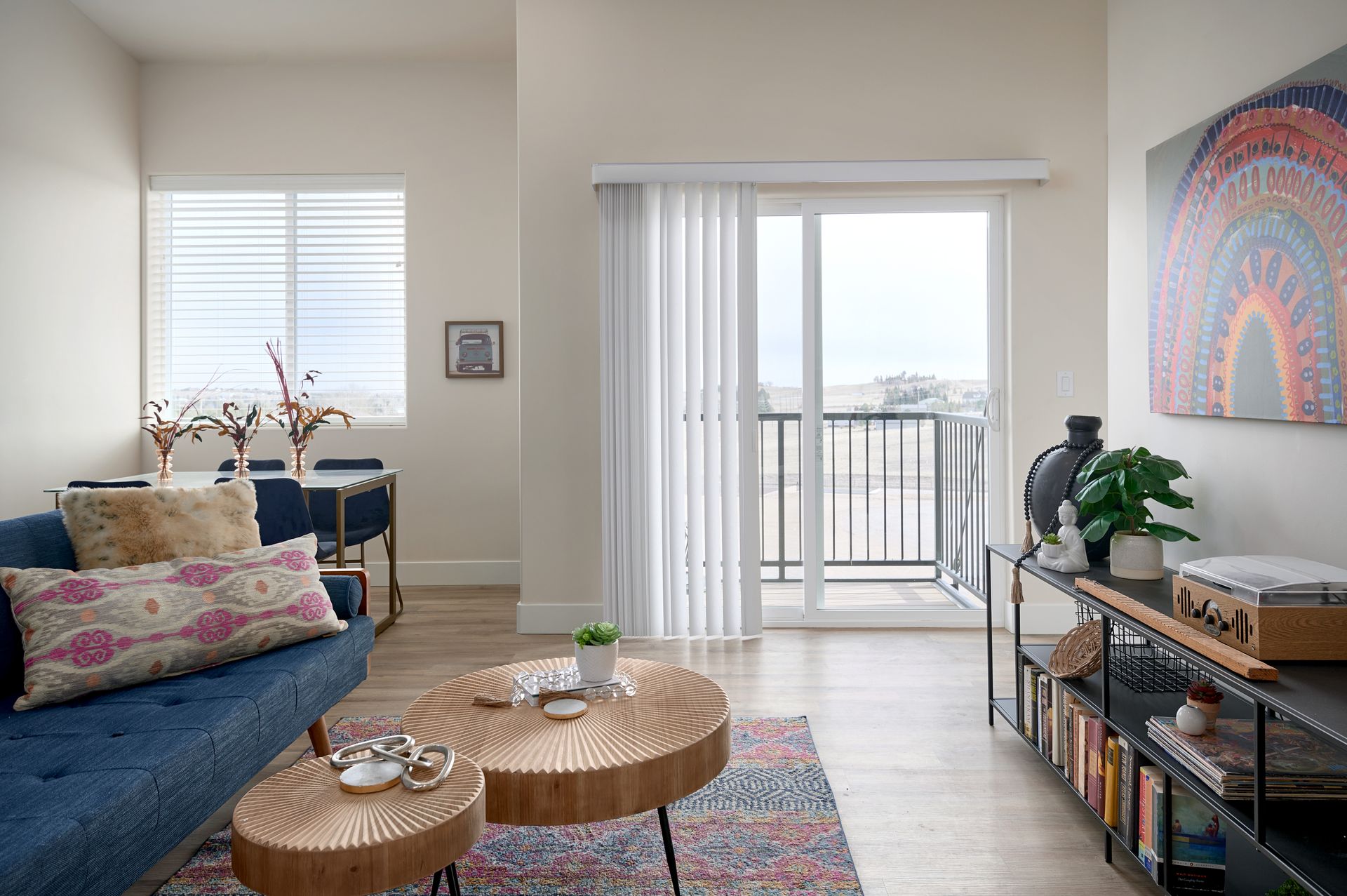 Bright living room with blue sofa, round wicker tables, TV console, and balcony doors with city view