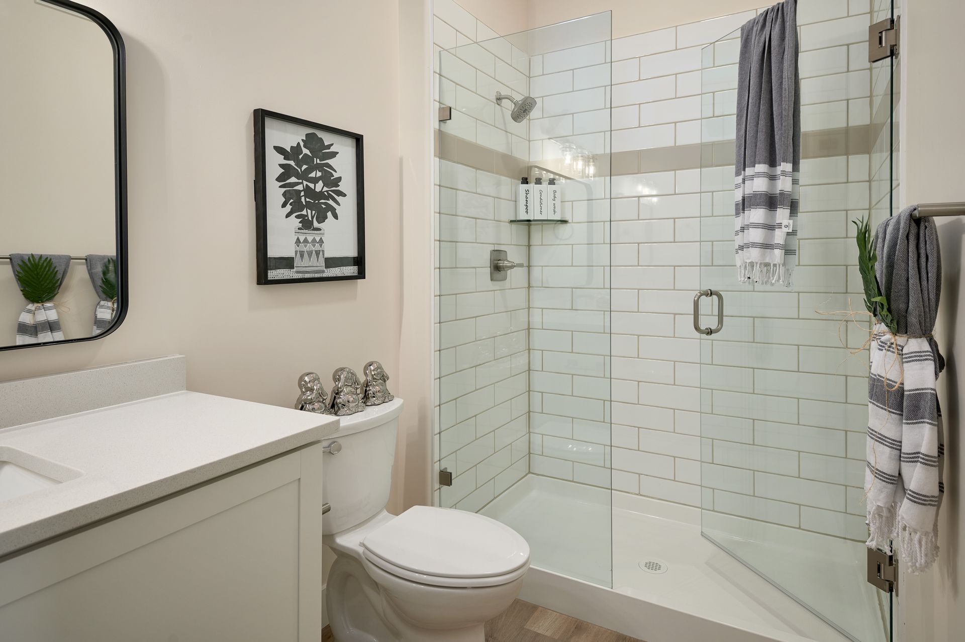 Small white bathroom with glass shower, toilet, vanity, and striped towels