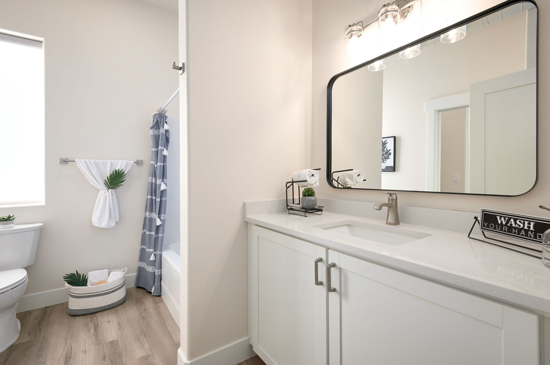 Modern bathroom vanity with large mirror, white cabinets, and tiled shower area in soft neutral tones
