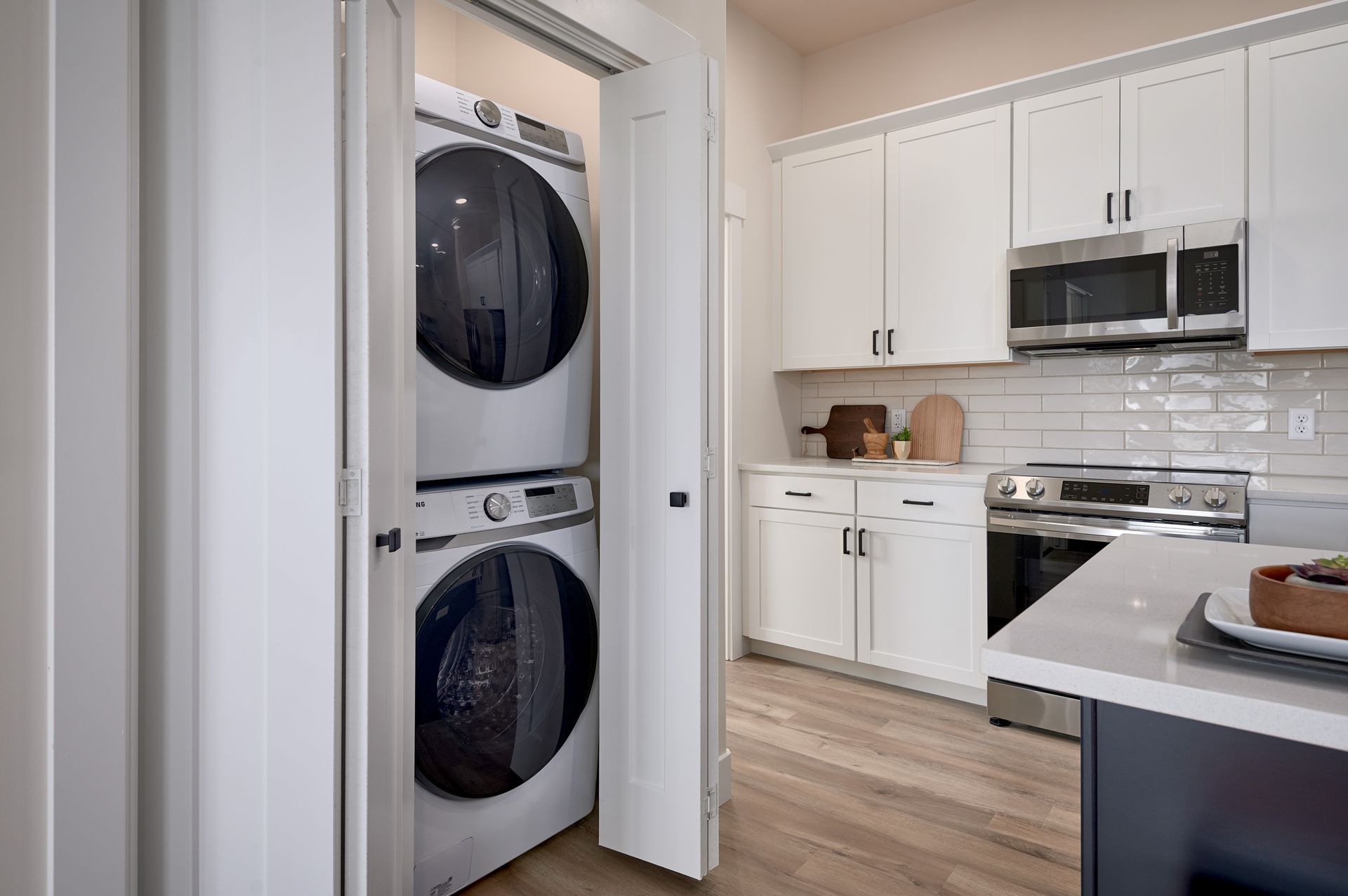 Stacked washer and dryer in a narrow laundry closet beside a bright white kitchen