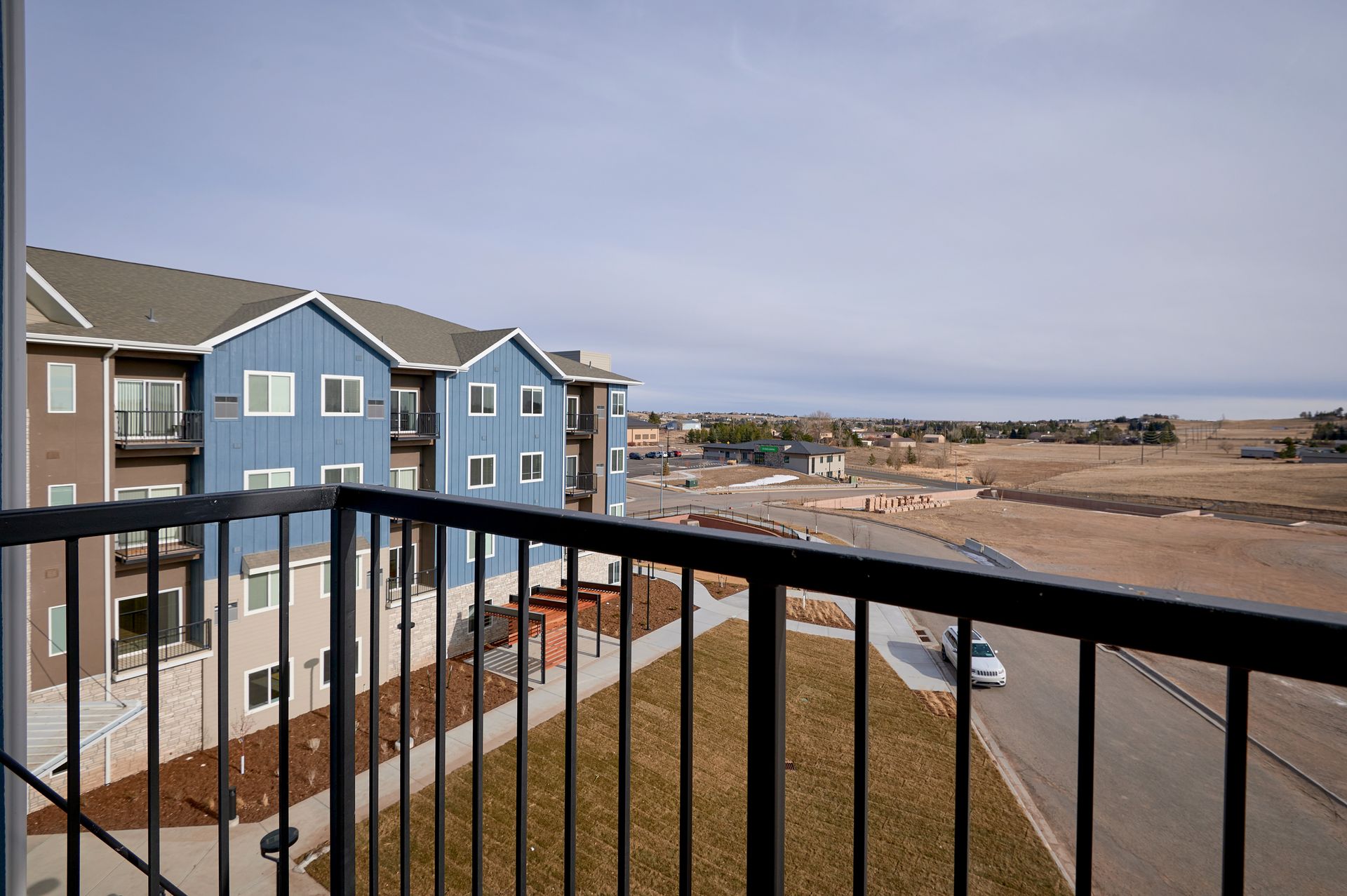 Balcony view of blue apartment buildings, sandy dunes, and ocean beyond a black railing