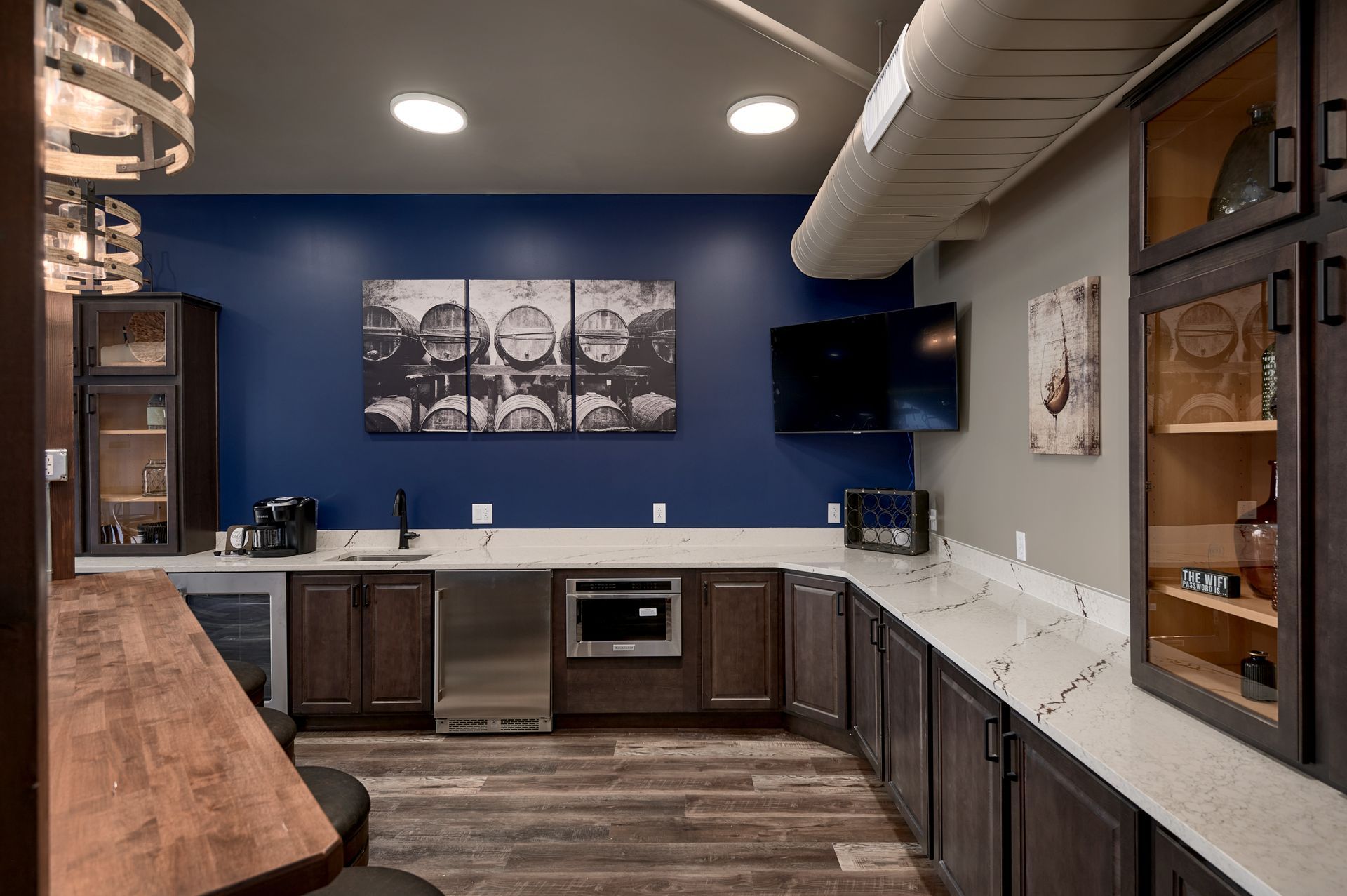 Modern kitchen with dark cabinets, blue accent wall, wood flooring, and a wall-mounted TV