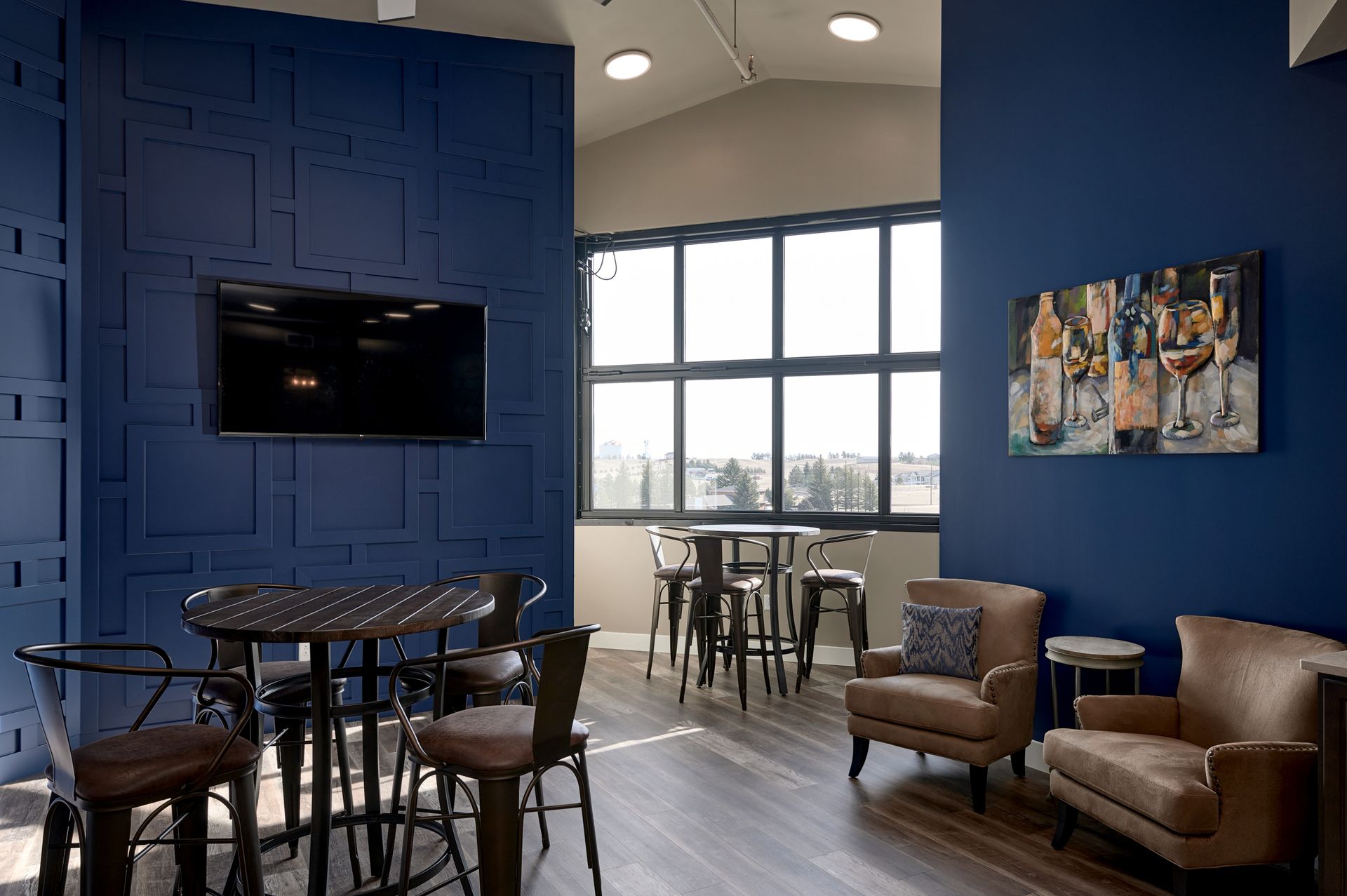 Modern lounge with blue walls, TVs, seating, and a large window overlooking a city view