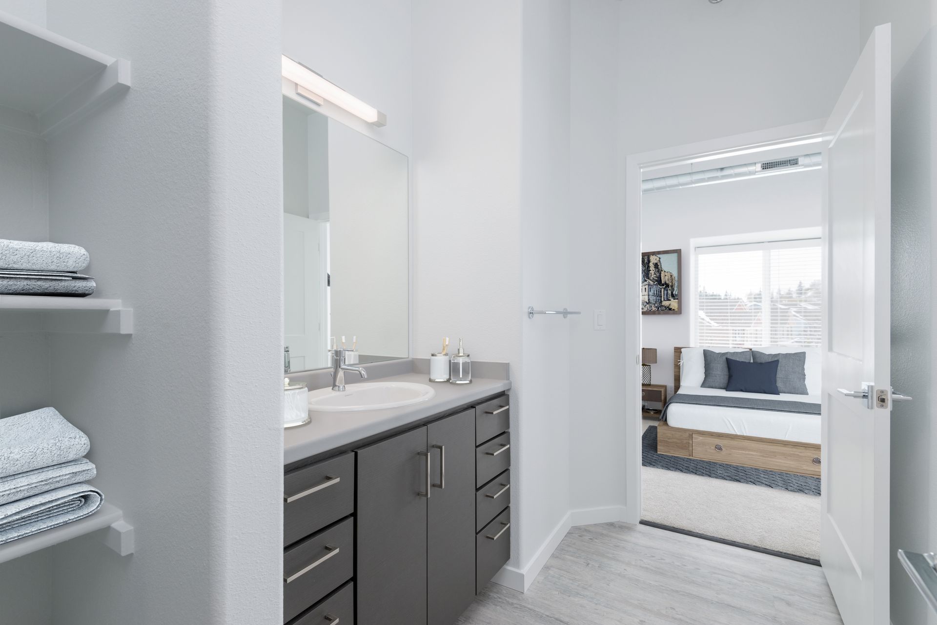 Bright bathroom with gray vanity, towels, and an open door to a bedroom and sitting area.