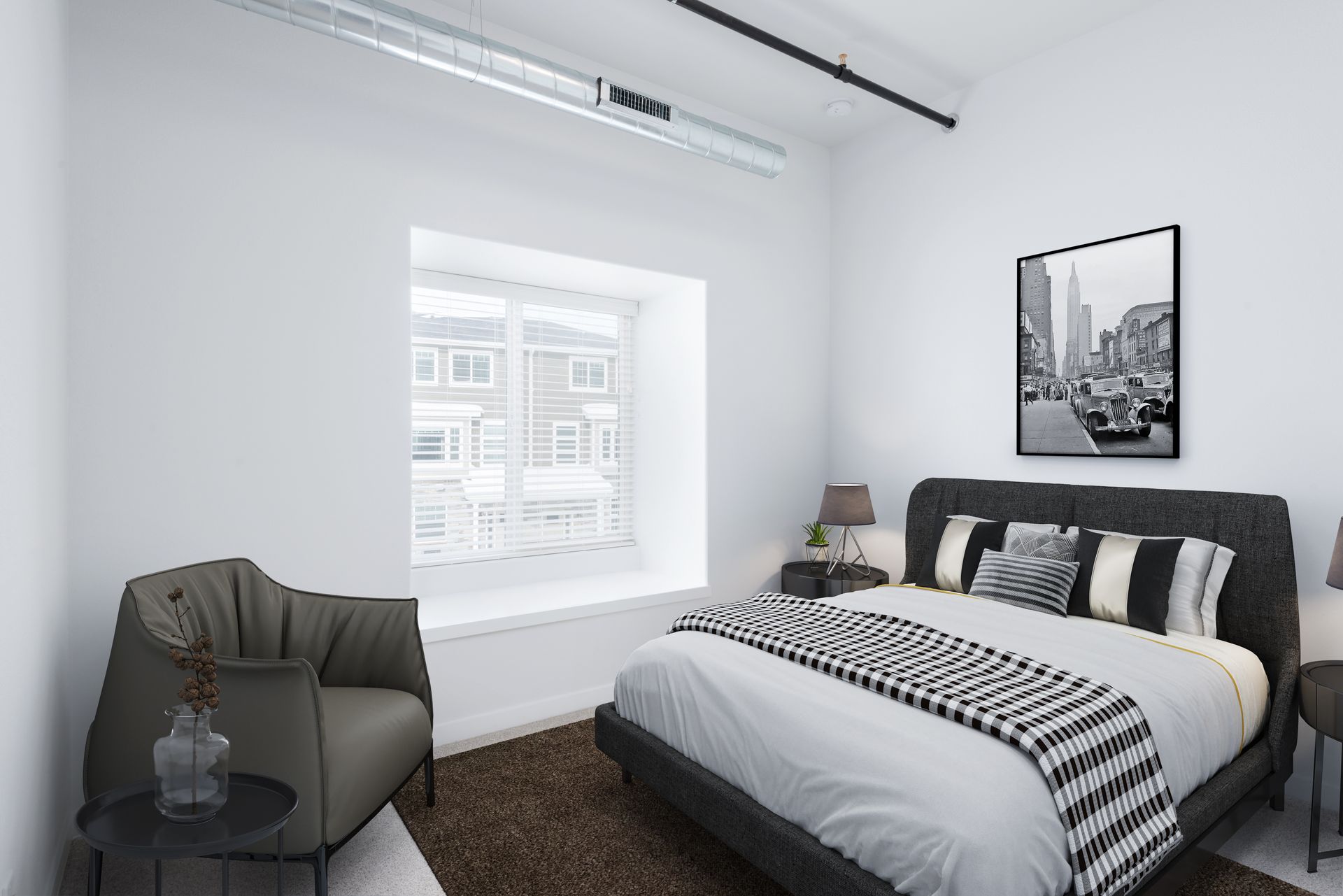 Modern bedroom with a bed, gray chair, black side table, and wall art beside a bright window.