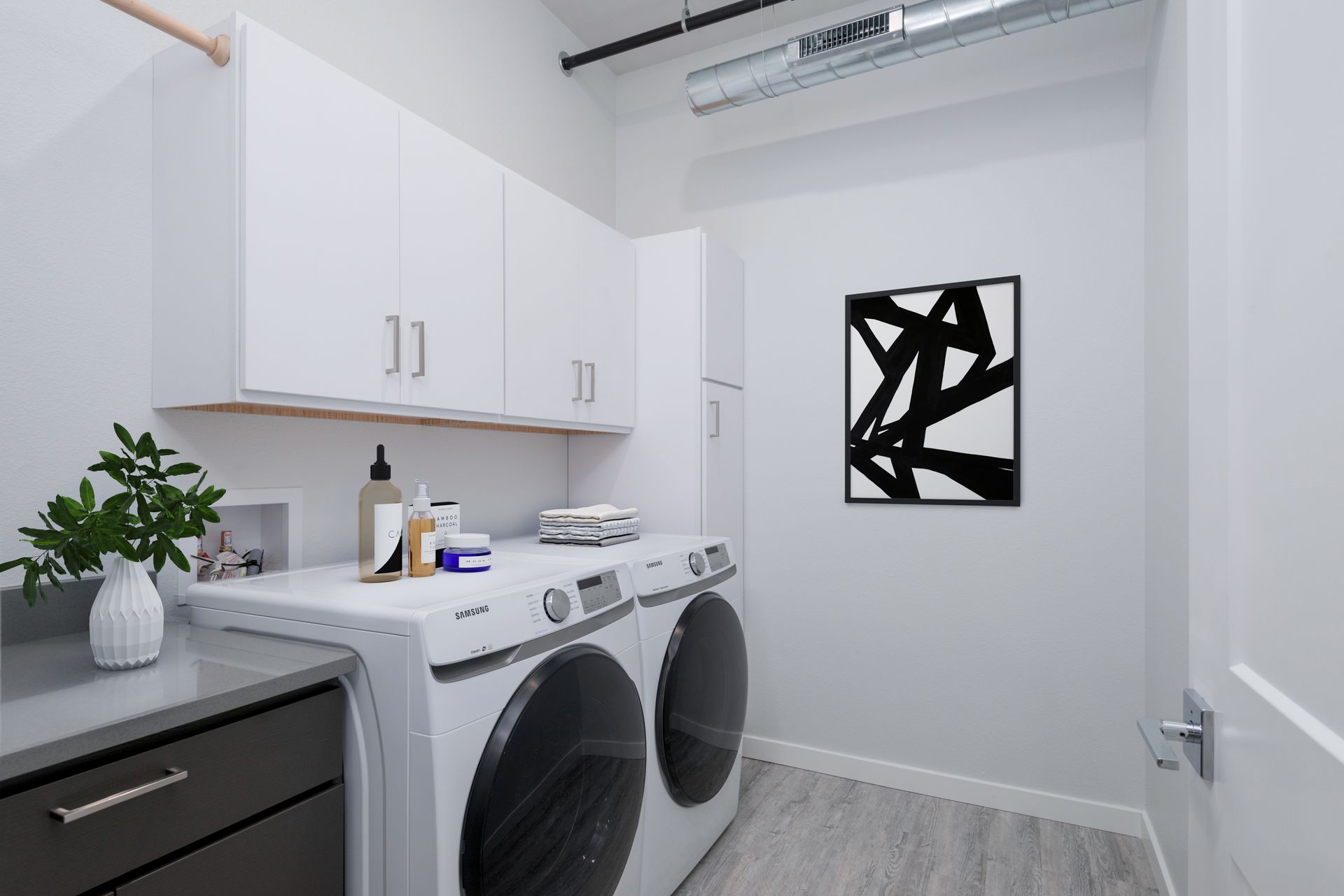 Bright laundry room with stacked washer and dryer, white cabinets, and abstract wall art.