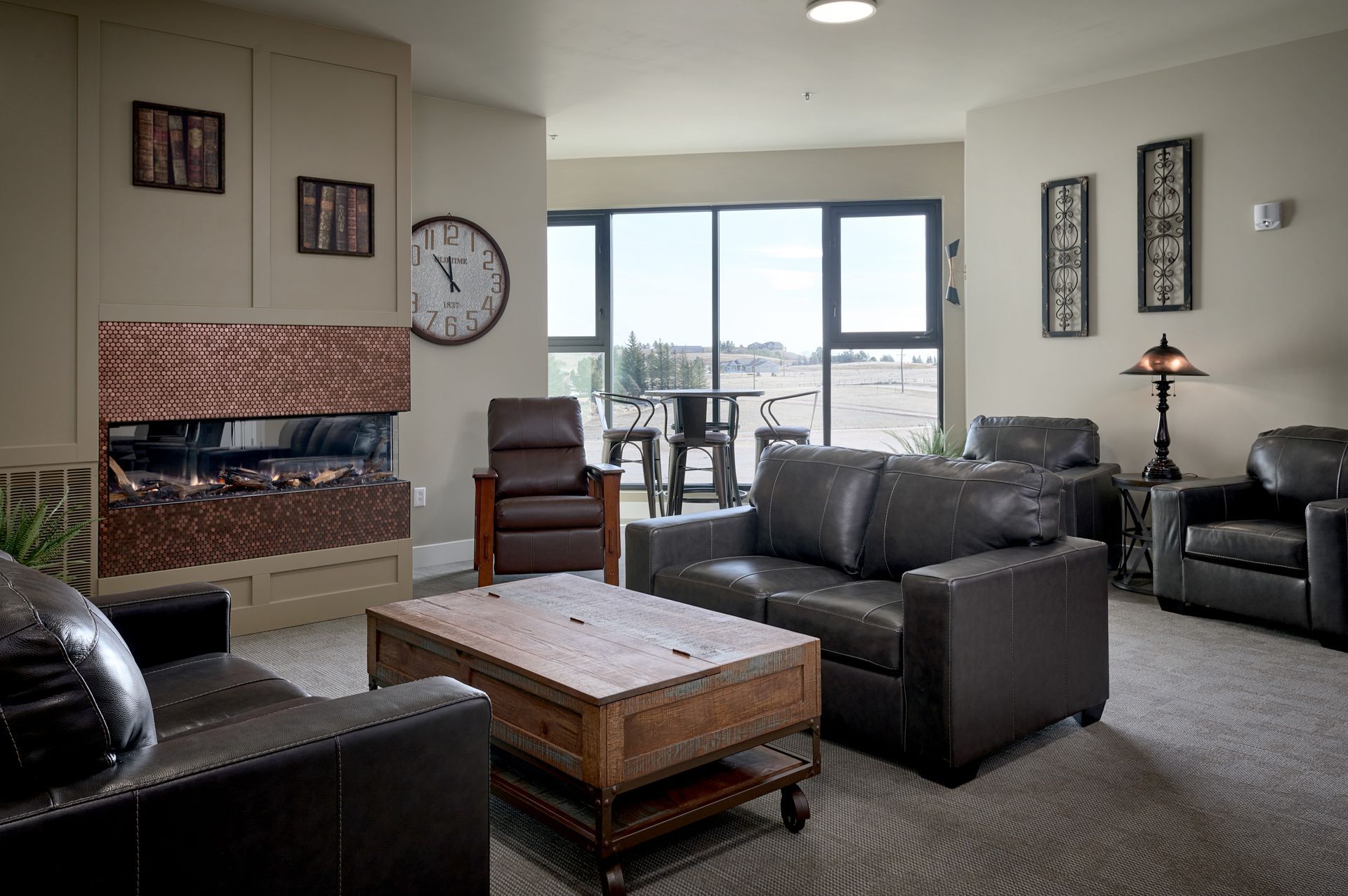 Cozy living room with gray seating, brick fireplace, wall clock, and large windows overlooking a city view