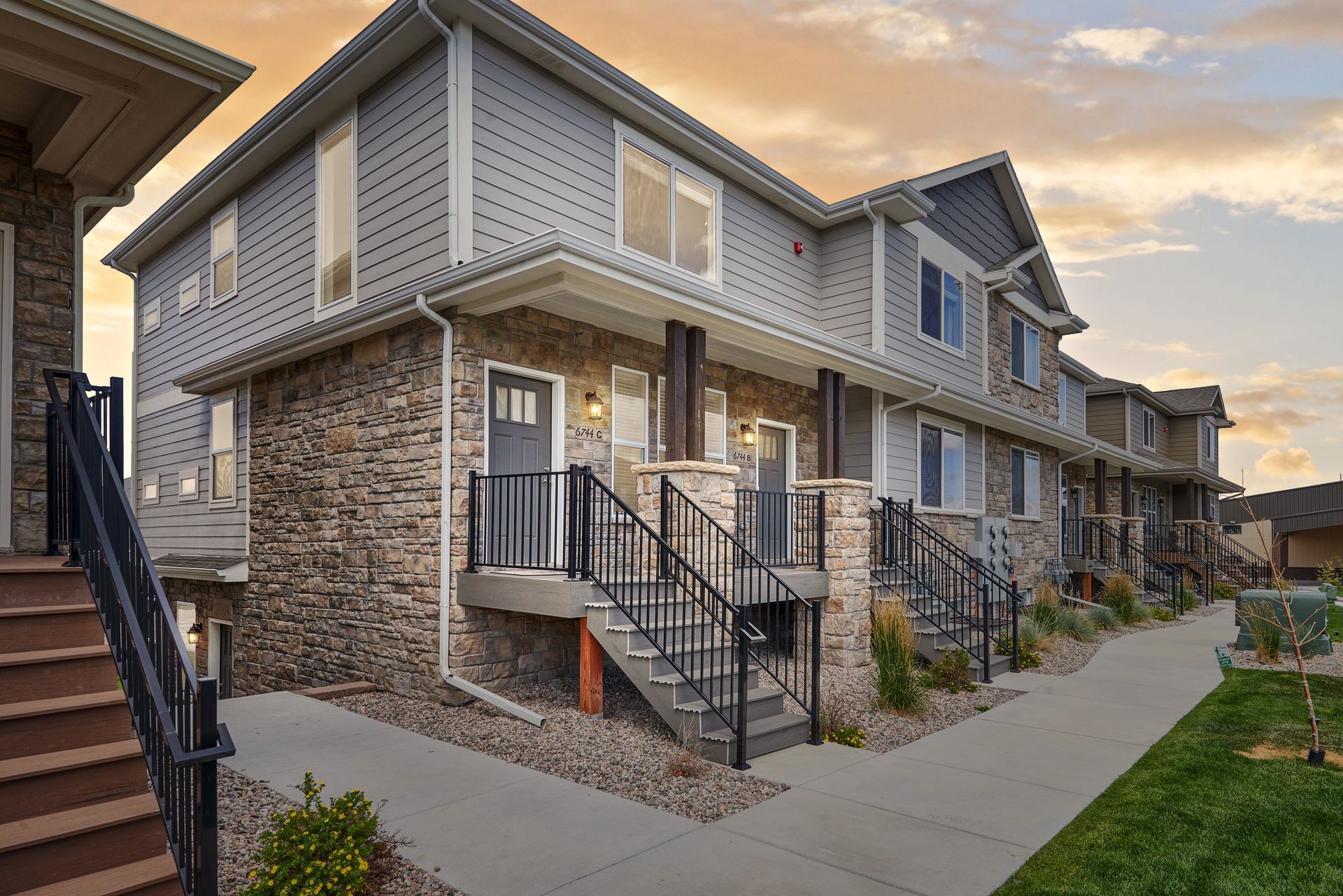 Row of modern apartment townhomes with stone facades and front steps along a paved walkway at sunset