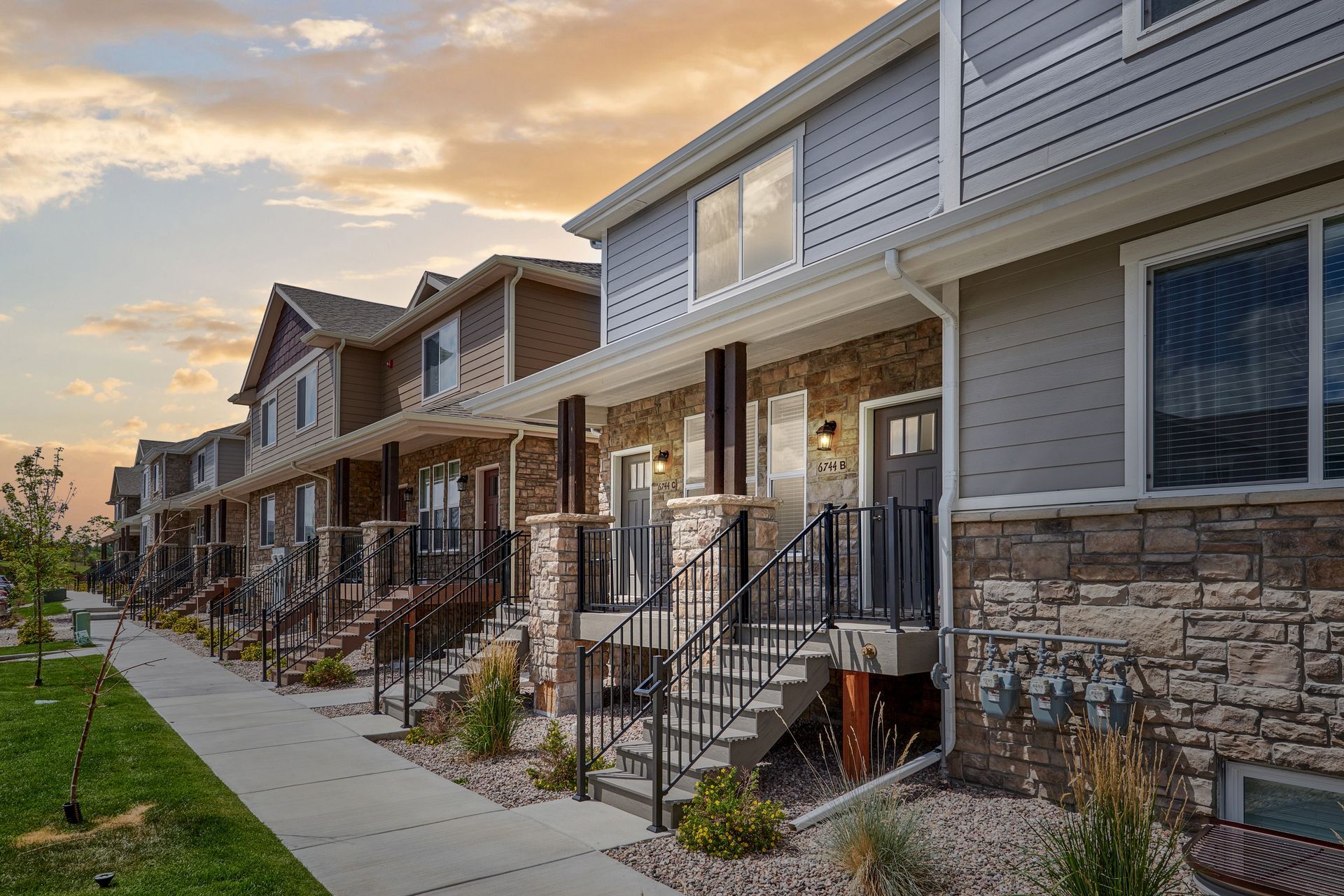 Row of modern townhouse homes with front porches along a sidewalk at sunset