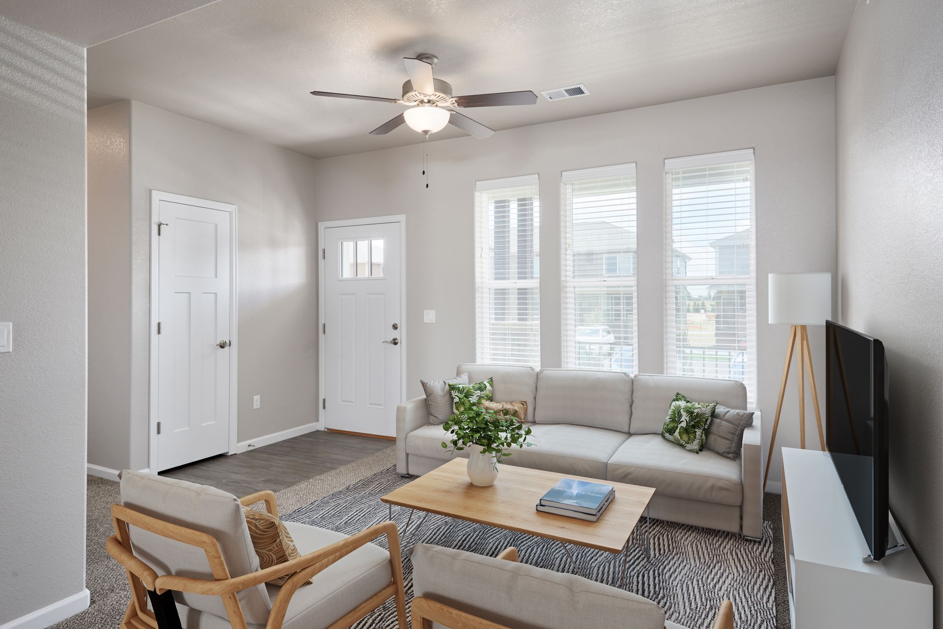 Bright living room with beige sofa, wood coffee table, chair, TV, and large windows.