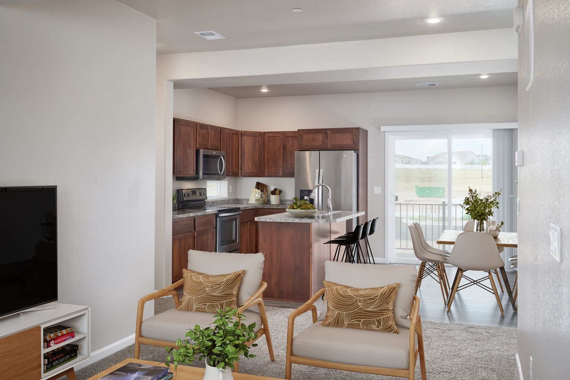 Bright open-plan living room with kitchen, dining table, and balcony doors overlooking greenery.