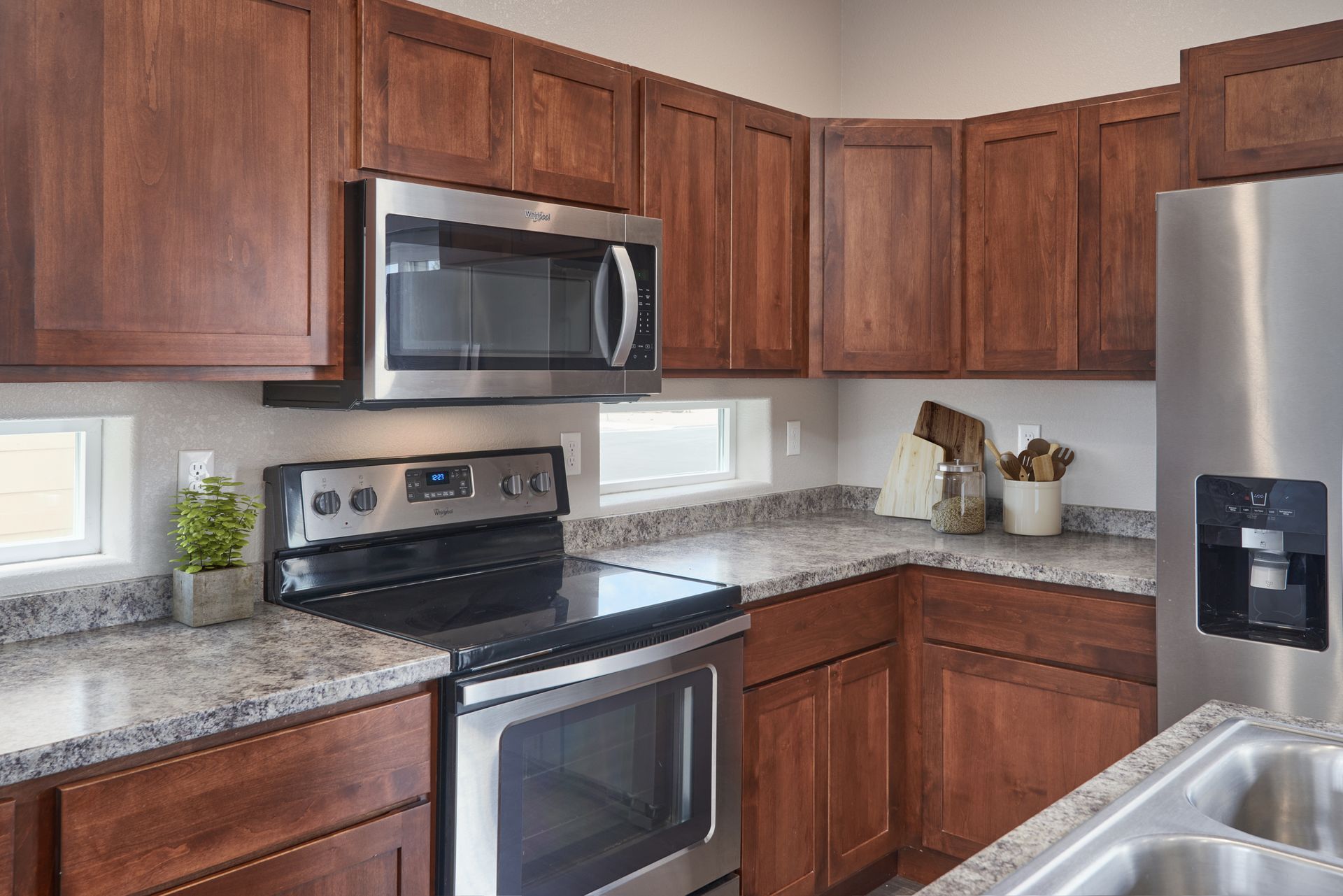 Modern kitchen with wood cabinets, stainless steel appliances, granite countertops, and a sink at right.