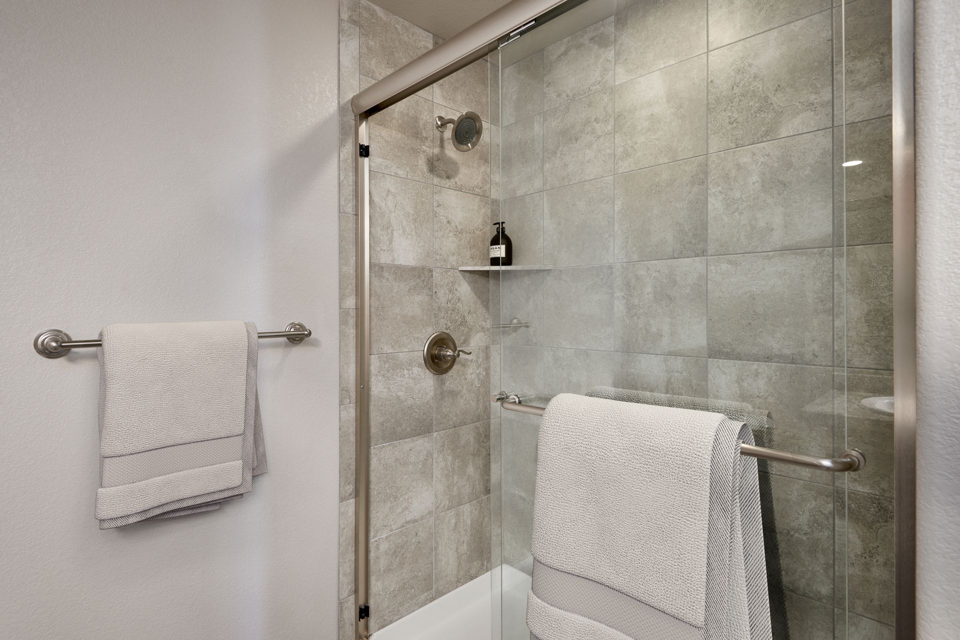 Bathroom shower with glass door, tiled walls, and two white towels hanging on bars.
