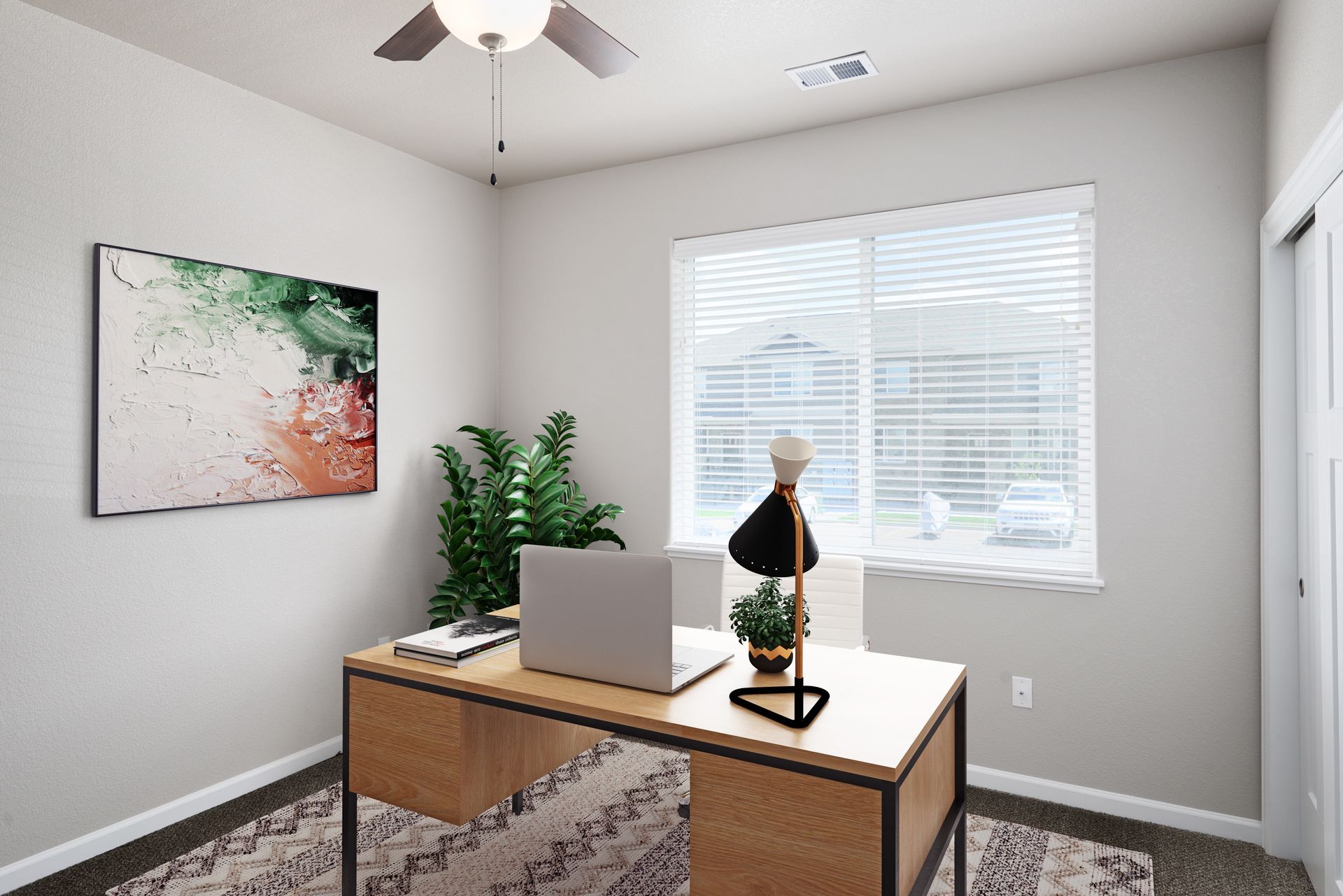 Modern home office with wooden desk, laptop, potted plant, wall art, and window blinds.