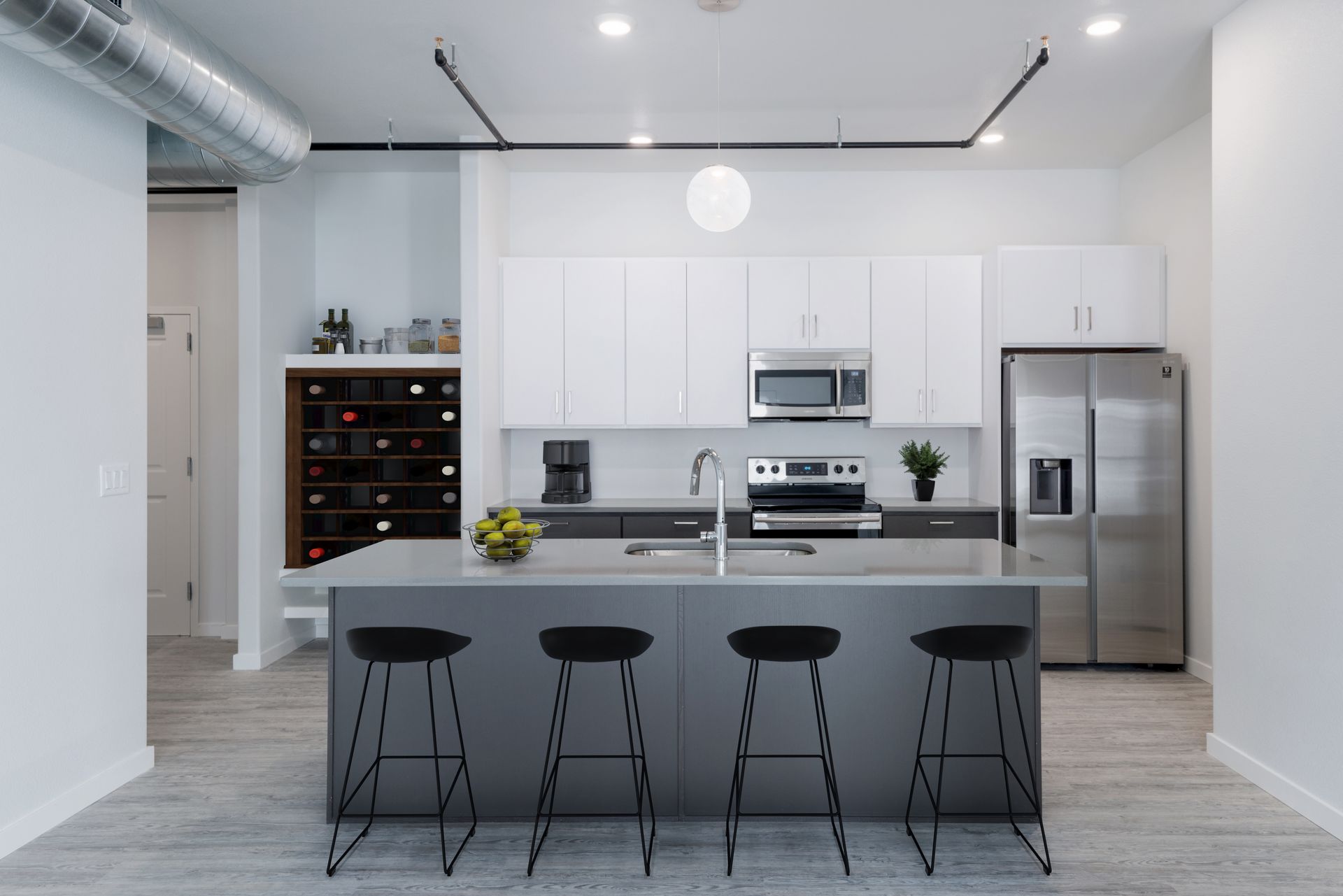 Modern white kitchen with island, four stools, stainless steel appliances, and wine rack