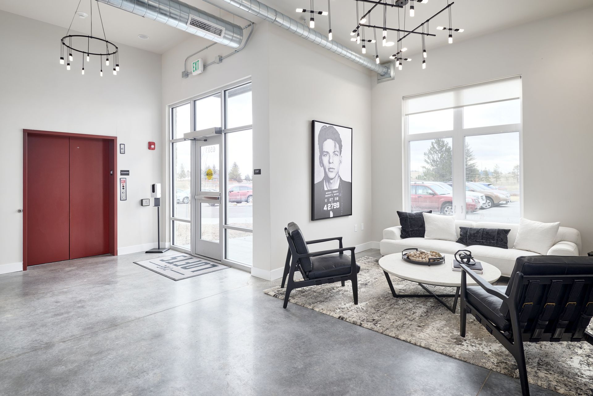 Bright modern lounge with red doors, large windows, black chairs, and white sofas on a rug.