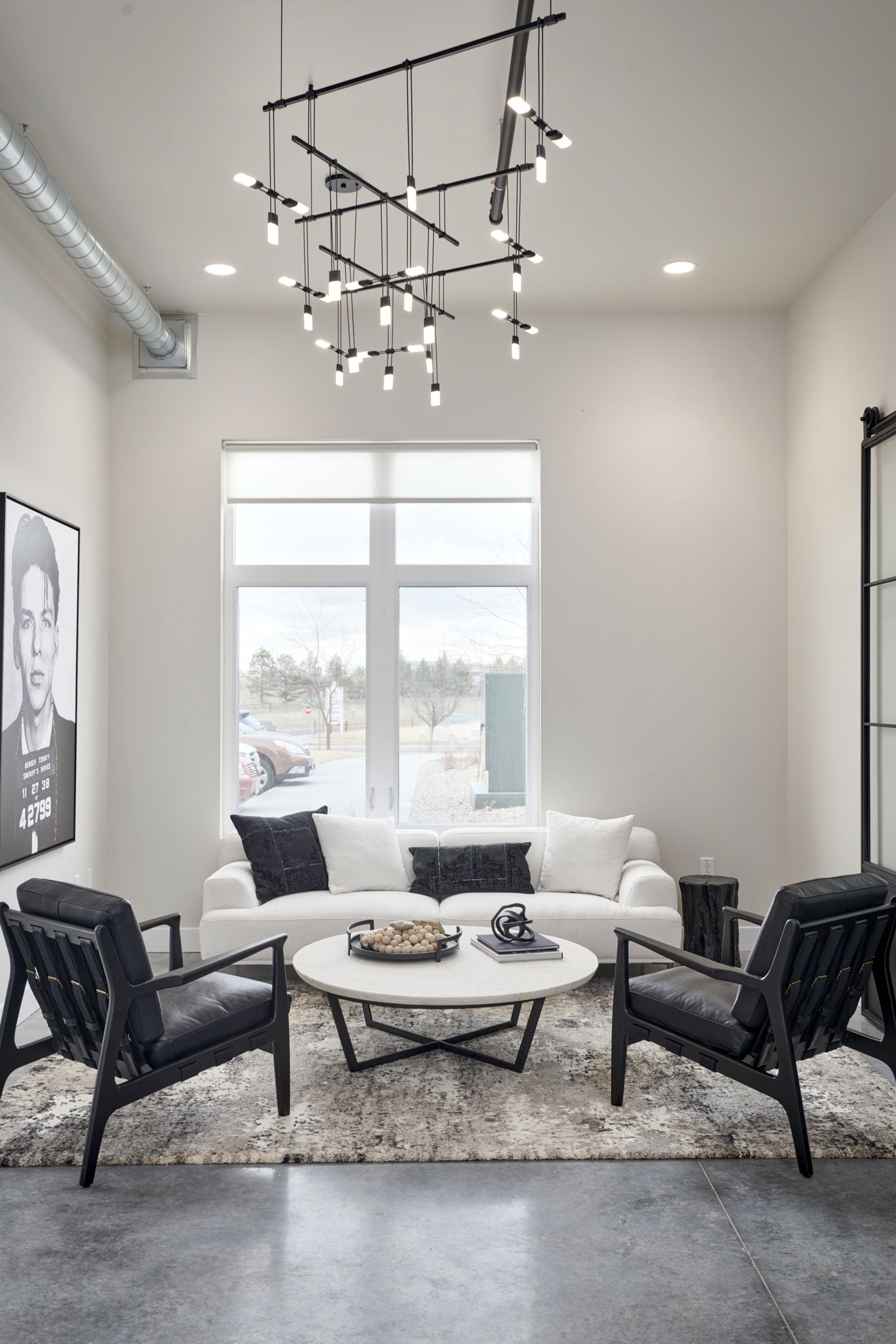 Modern sitting area with black chairs, white sofa, round coffee table, and large window under a contemporary chandelier