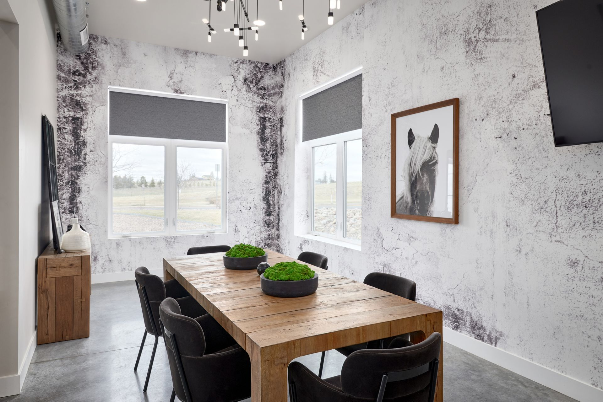 Modern dining room with a wooden table, black chairs, and large windows with gray blinds