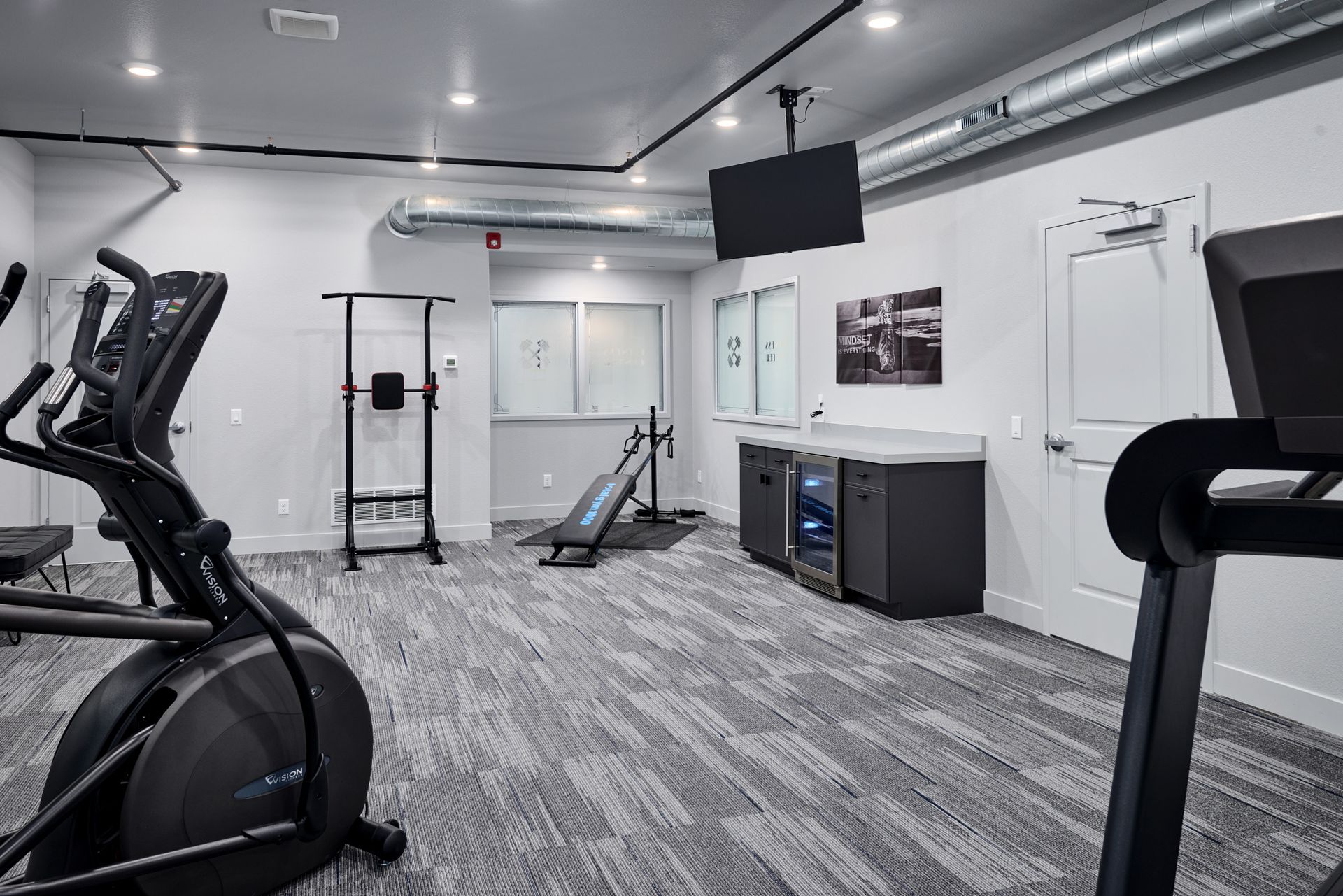 Modern gym with cardio machines, weight bench, mirrors, and TV in a bright, clean room